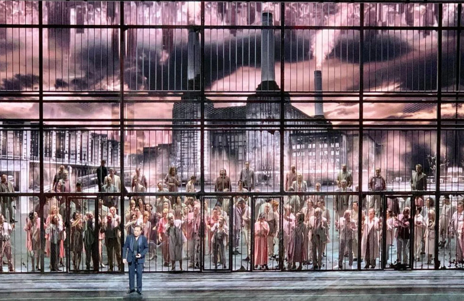 Chorus behind a tall grid of bars, a smoking industrial power station projected under pink skies – Macbeth at La Scala, Milan, Italy, 2021 – opera set design