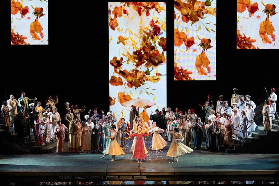 Lakmé scene with full chorus on stairs, dancers in yellow and red and screens of falling autumn leaves – Lakmé at the Royal Opera House Muscat, Oman, 2019 – set design