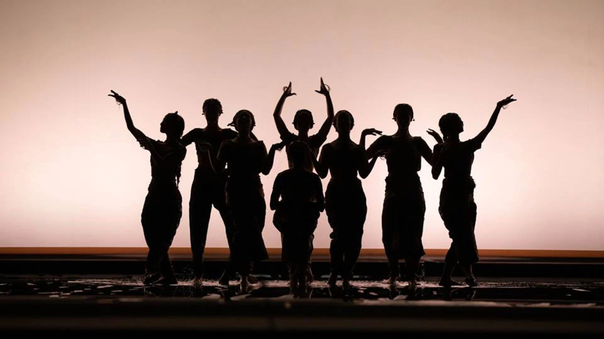 Line of dancers in silhouette with raised arms against a softly glowing pink backdrop – Lakmé at the Royal Opera House Muscat, Oman, 2019 – set design