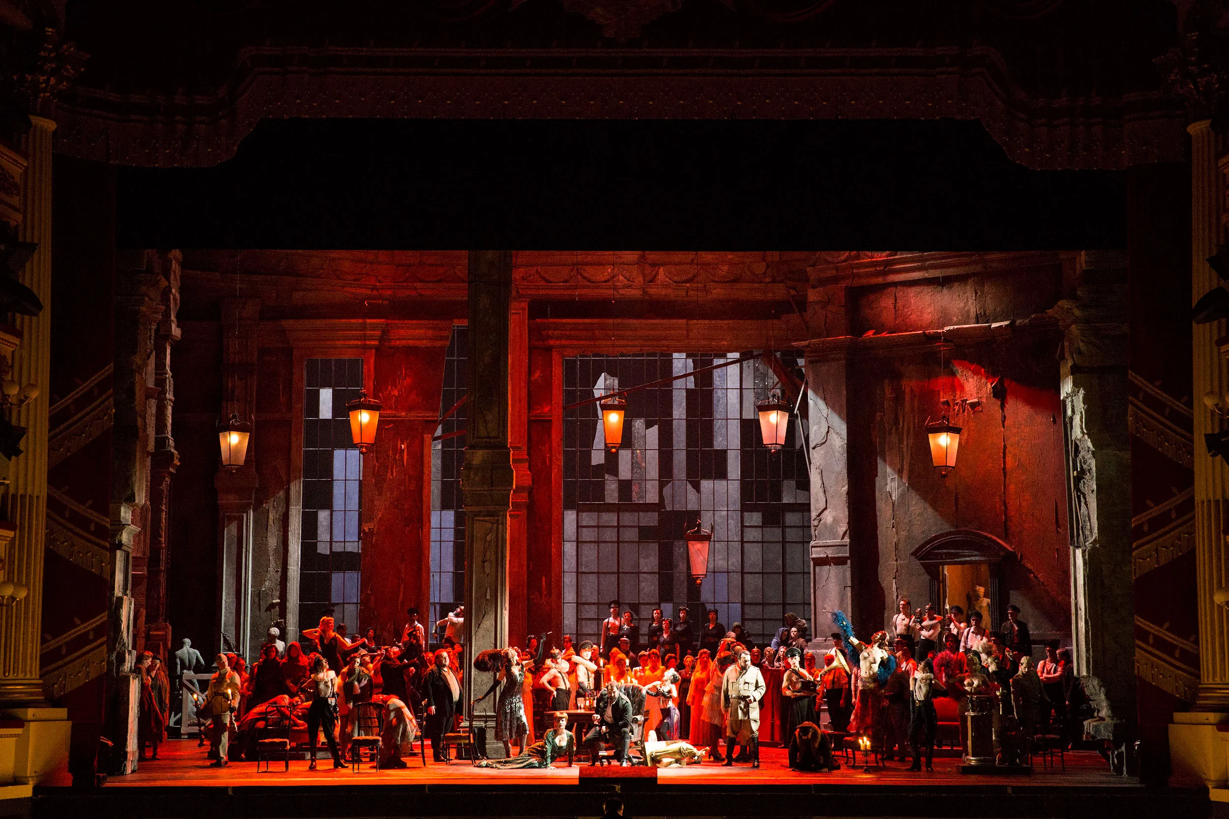 Crowded banquet scene in red light inside the ruined palace, lanterns hanging overhead – Attila at La Scala, Milan, Italy, 2018 – opera set design