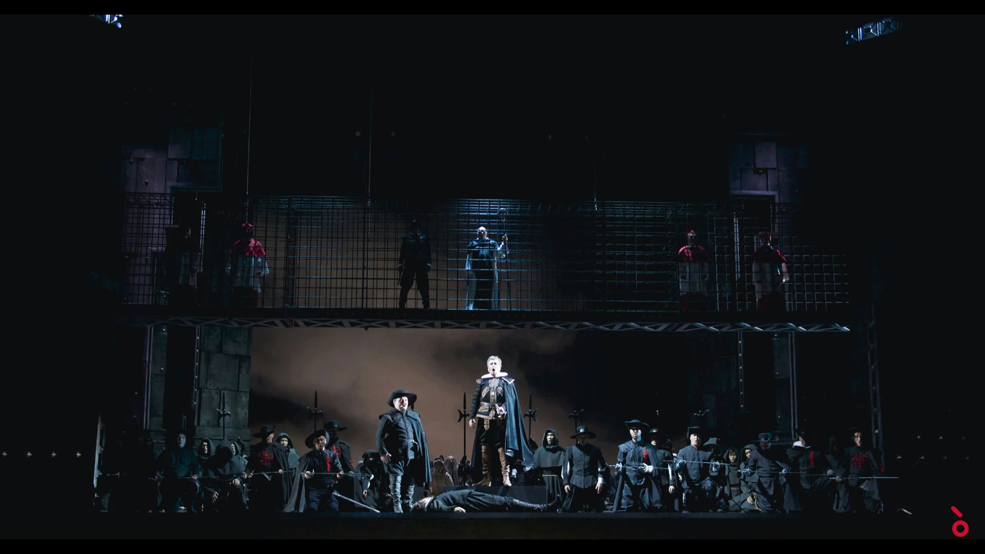 Soldier figures below a two-level iron cage set, a man lying on the stage floor in front – Don Carlo at Astana Opera, Kazakhstan, 2023 – set design