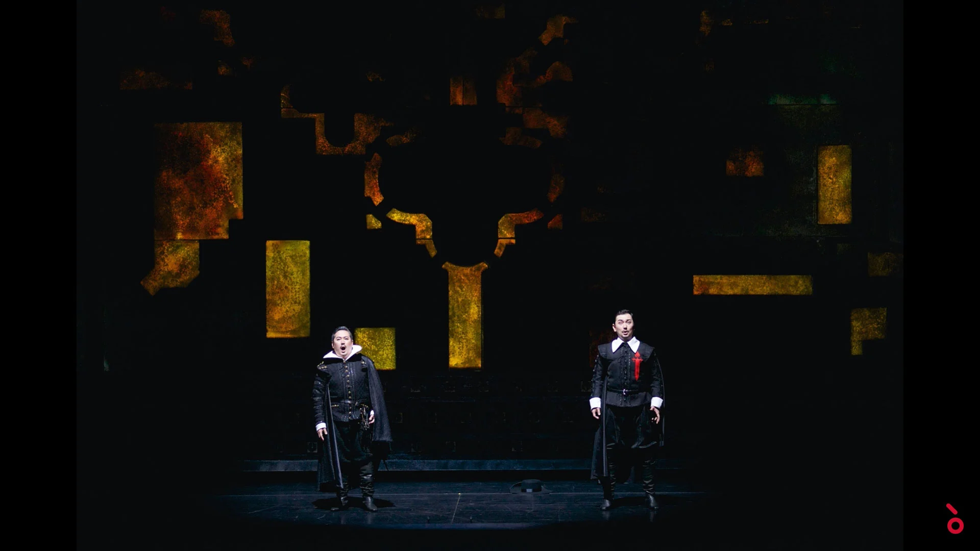 Two singers in black Spanish costume on a dark stage with golden fragments of a cross behind – Don Carlo at Astana Opera, Kazakhstan, 2023 – set design