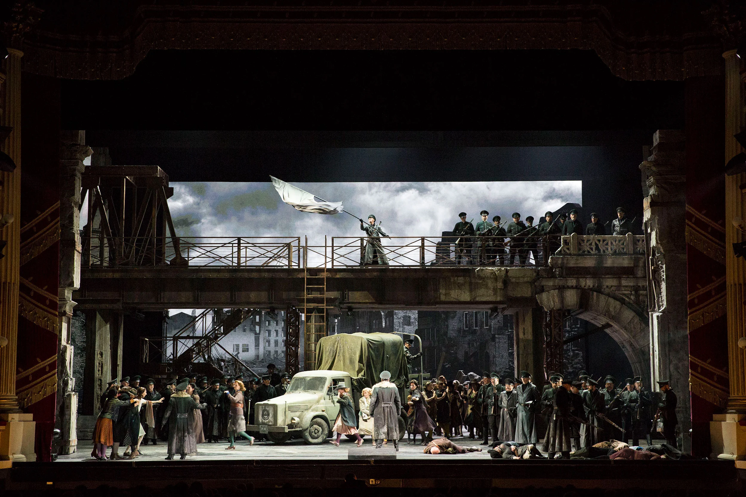 Monumental bridge with soldiers and a waving flag above a crowd and a military truck – Attila at La Scala, Milan, Italy, 2018 – opera set design