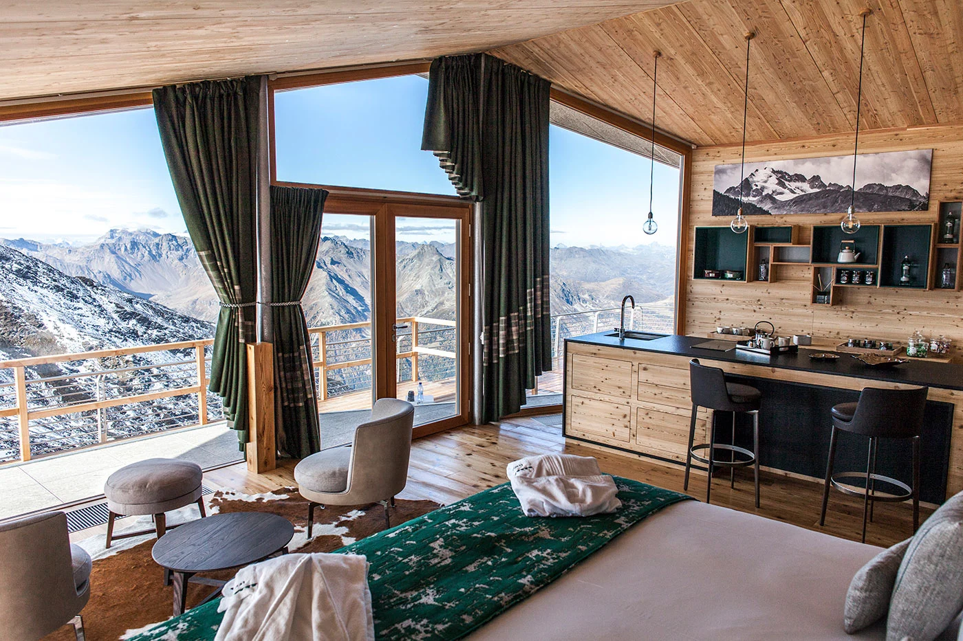 Chalet suite with a bed, armchairs and kitchen bar under a wooden ceiling, full-height windows onto the mountains – Levissima 3000 Chalet, Valdisotto, Italy, 2018 – architecture