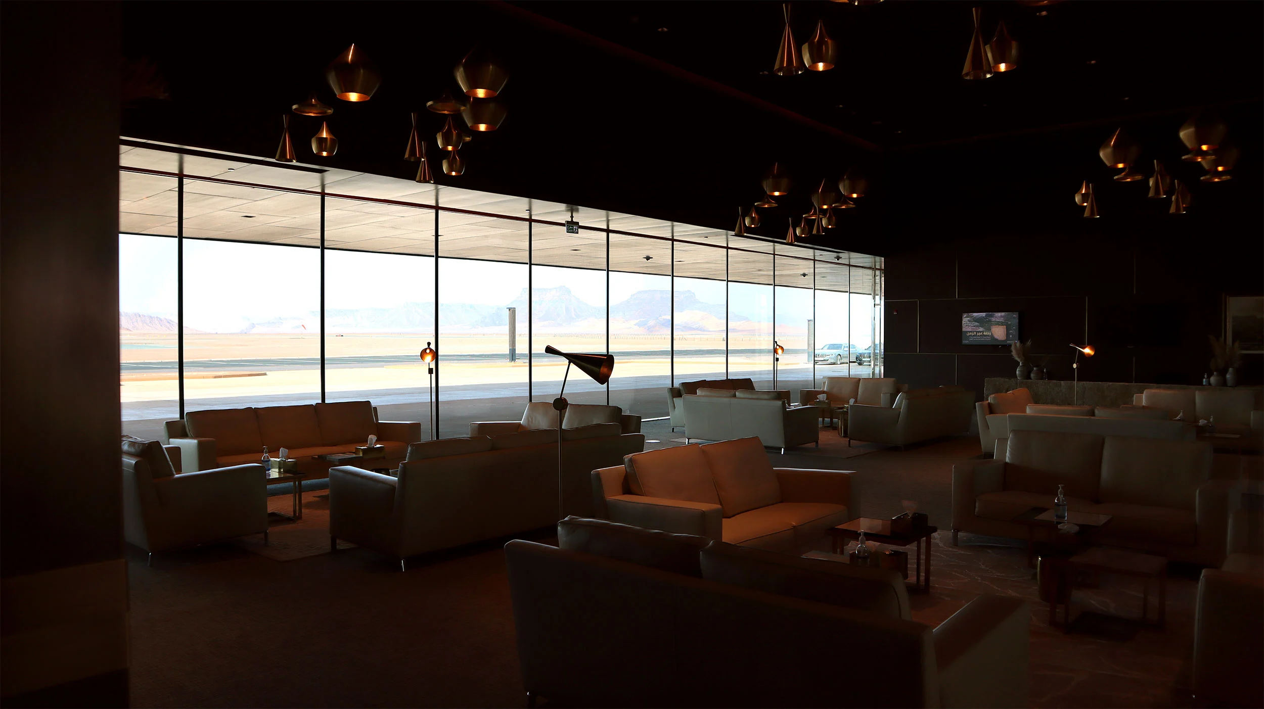 Lounge with leather sofas and copper pendant lamps, full-height glazing onto the airfield – Prince Abdul Majeed bin Abdulaziz Airport, AlUla, Saudi Arabia, 2021 – architecture