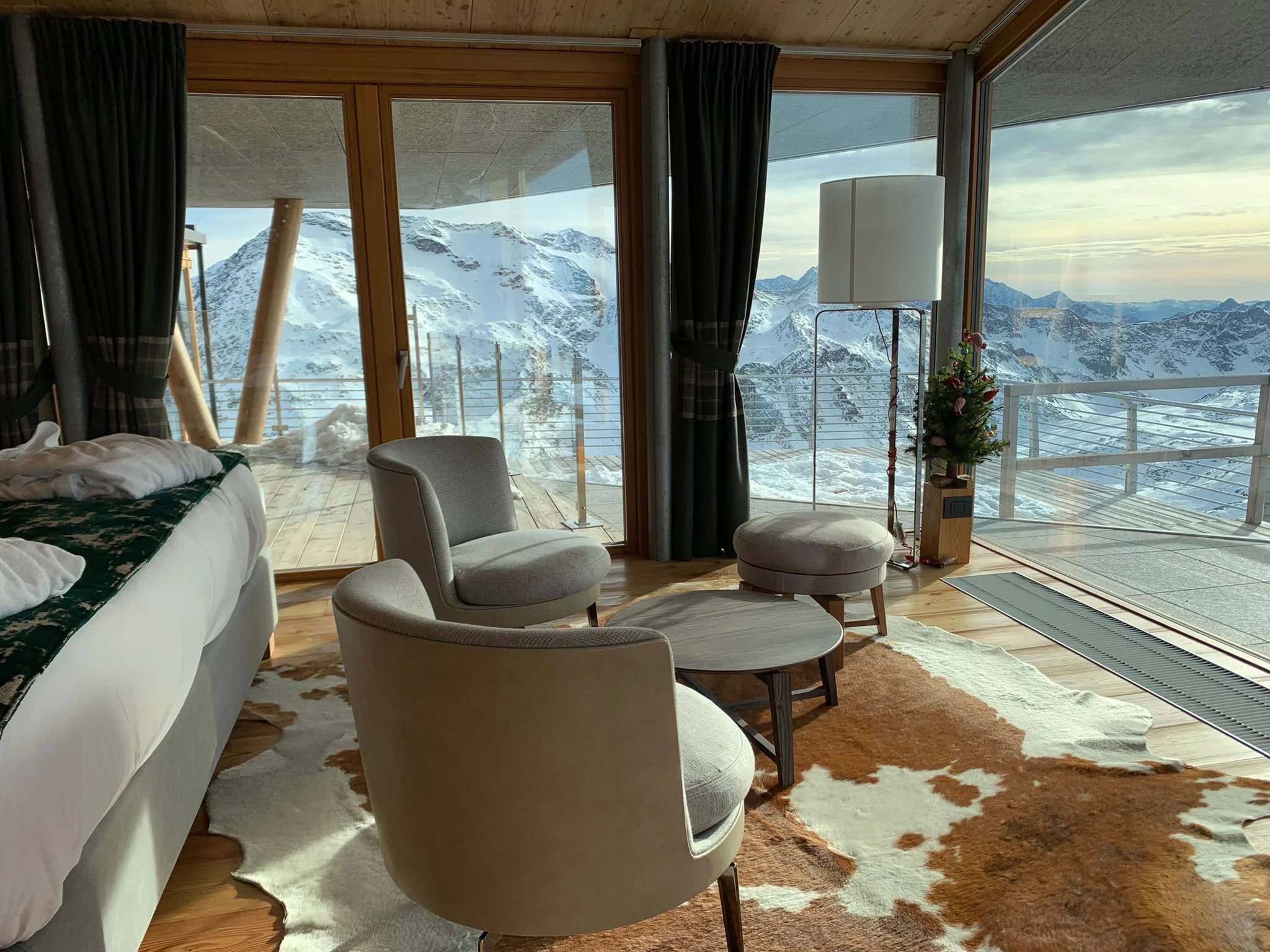 Bedroom seating corner with grey armchairs on a cowhide rug, glass walls opening onto the terrace and Alps – Levissima 3000 Chalet, Valdisotto, Italy, 2018 – architecture