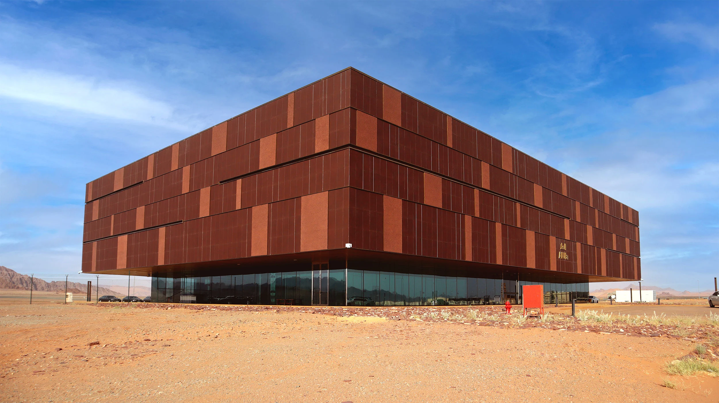 The terminal's cantilevered volume clad in reddish panels, floating above a glazed base in the desert – Prince Abdul Majeed bin Abdulaziz Airport, AlUla, Saudi Arabia, 2021 – architecture