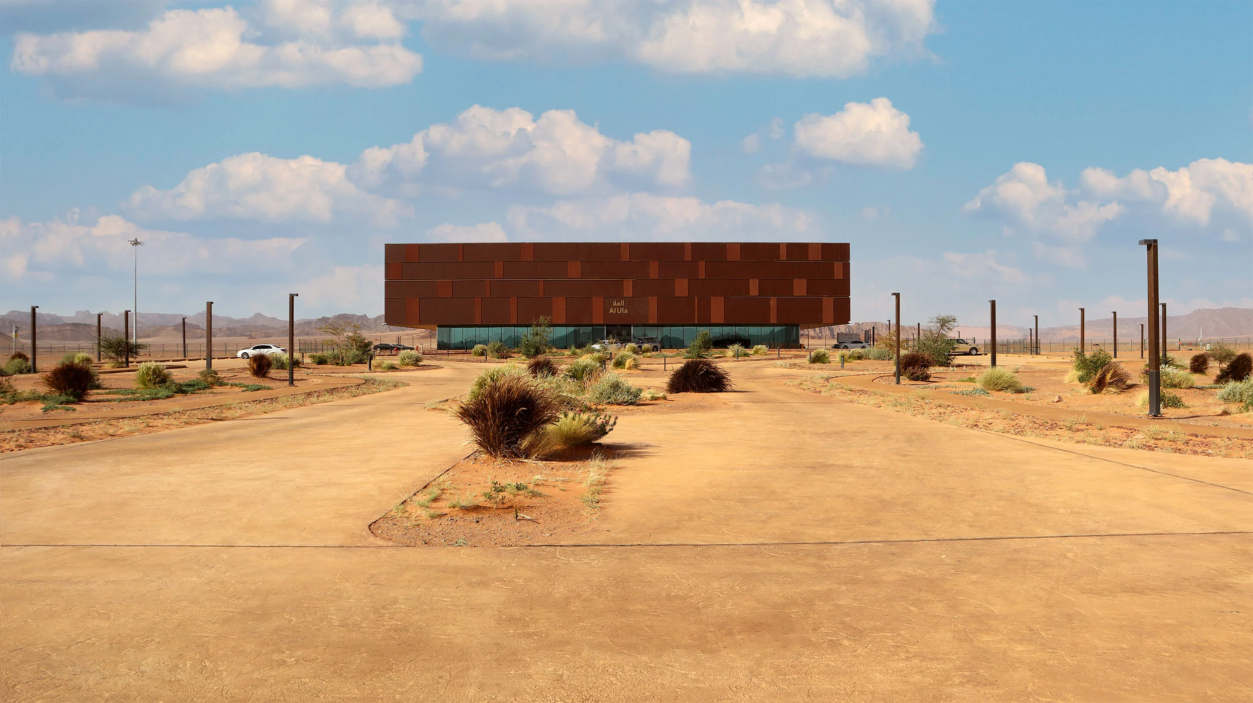 Distant front view of the terminal across a curving desert approach road planted with shrubs – Prince Abdul Majeed bin Abdulaziz Airport, AlUla, Saudi Arabia, 2021 – architecture