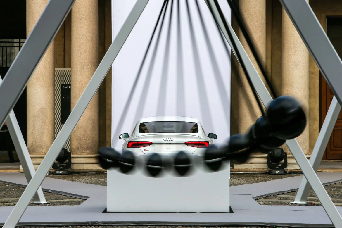 White Audi on a plinth seen through a steel frame, with a swinging black pendulum in motion – Audi City Lab at Fuorisalone, Milan, Italy, 2017 – event design