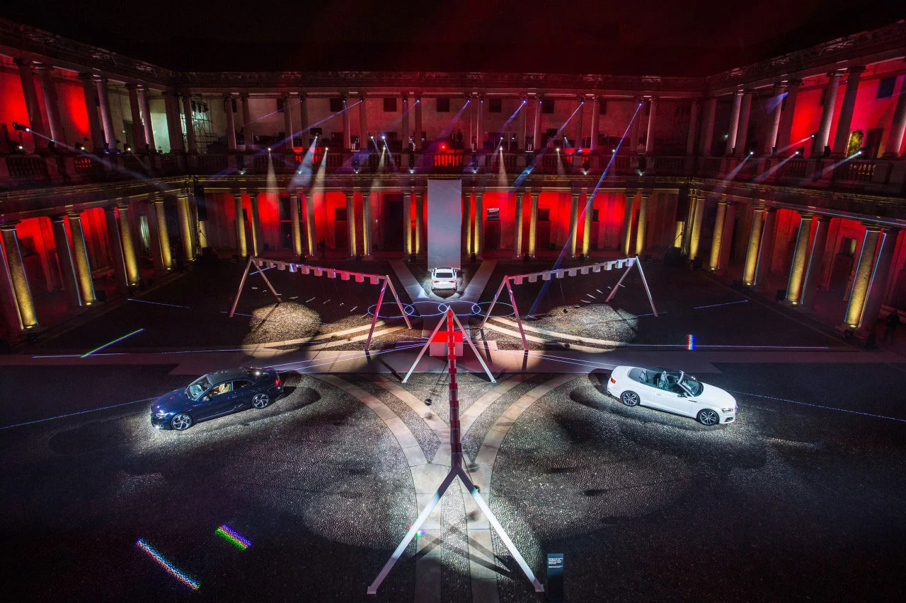 High view of the courtyard installation: two convertibles in spotlights and tall white swing frames – Audi City Lab at Fuorisalone, Milan, Italy, 2017 – event design