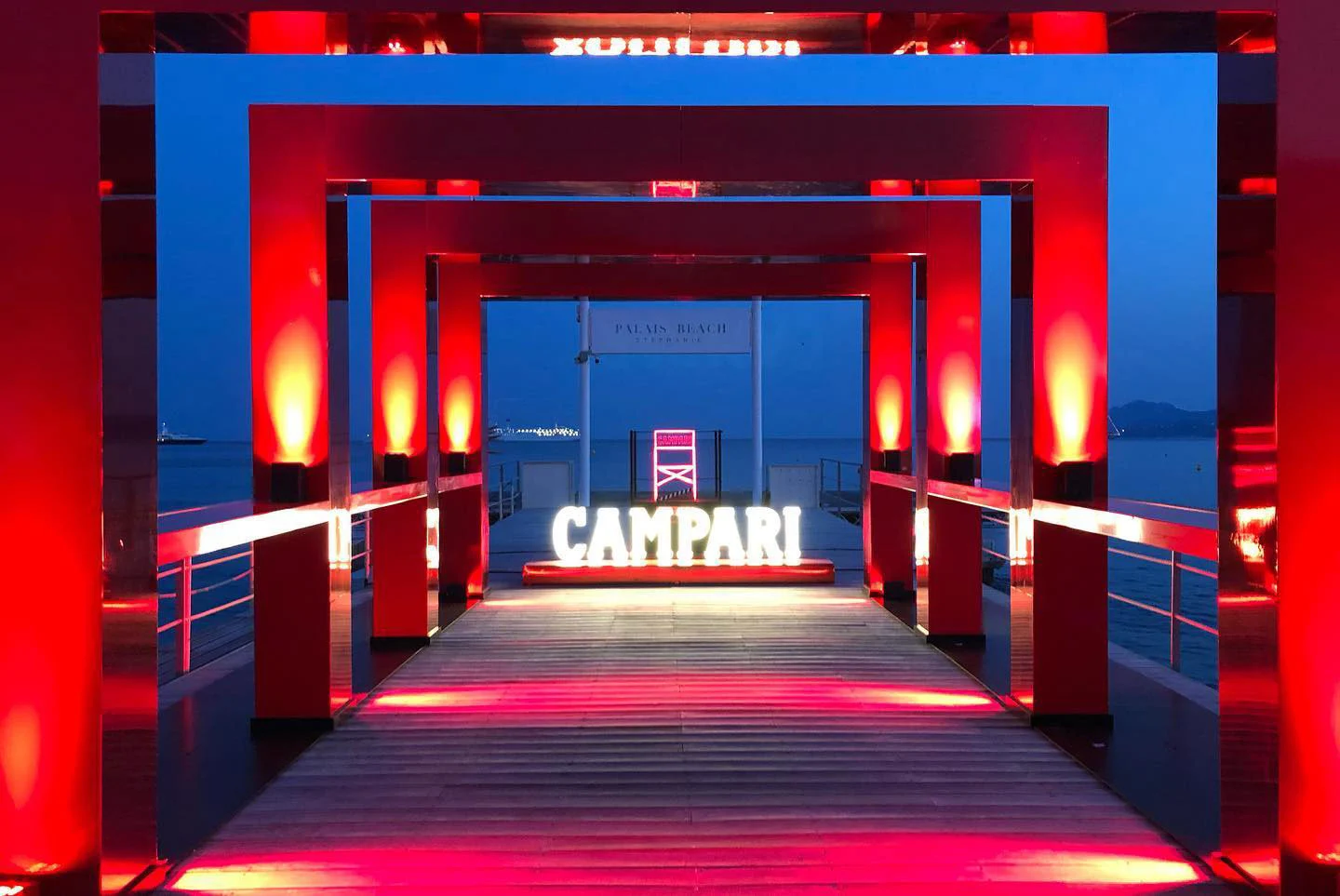 Pier lined with red-lit portal frames leading to a glowing Campari sign above the sea at dusk – Campari at the 75th Cannes Film Festival, France, 2022 – event design