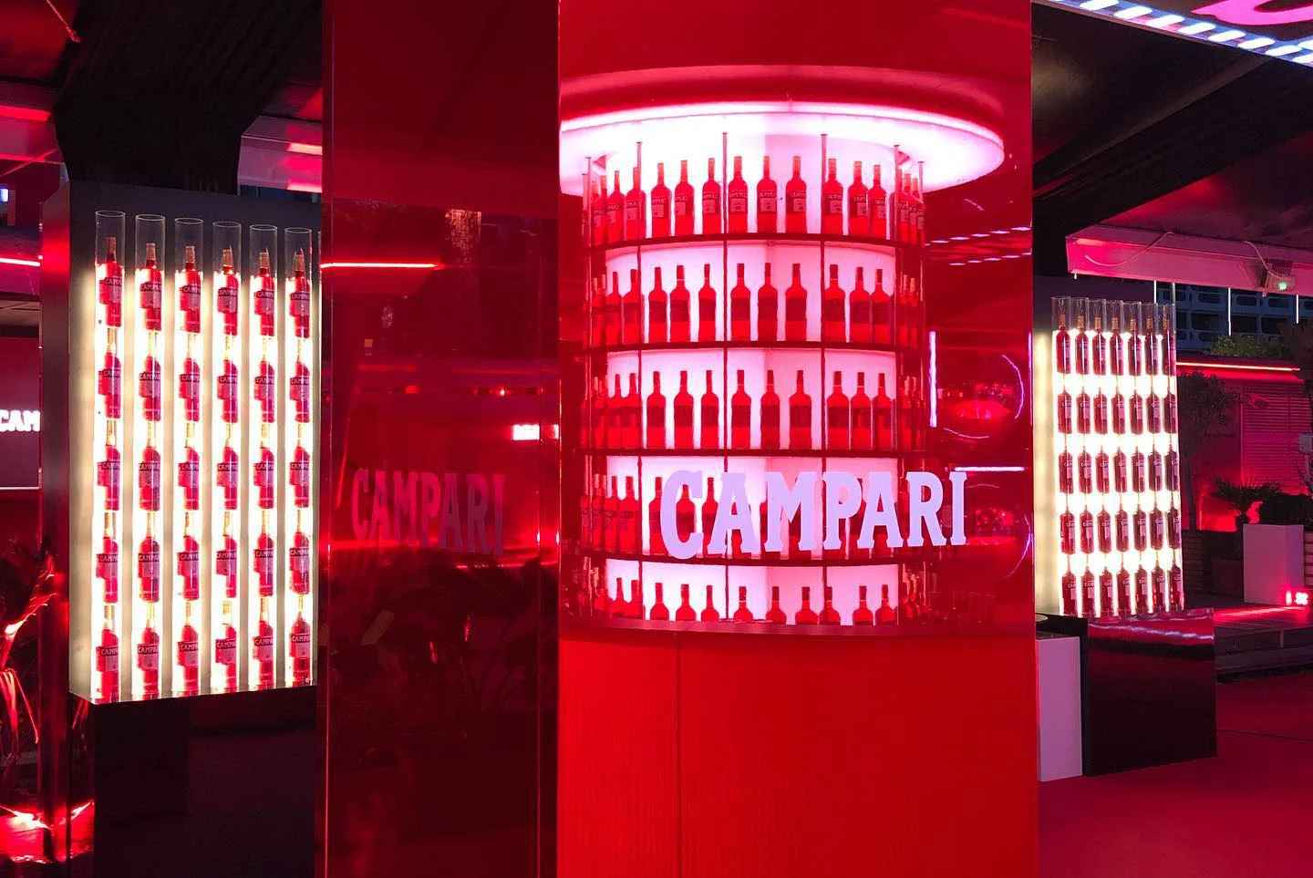 Backlit shelves of Campari bottles on a cylindrical display and wall columns in red light – Campari at the 75th Cannes Film Festival, France, 2022 – event design