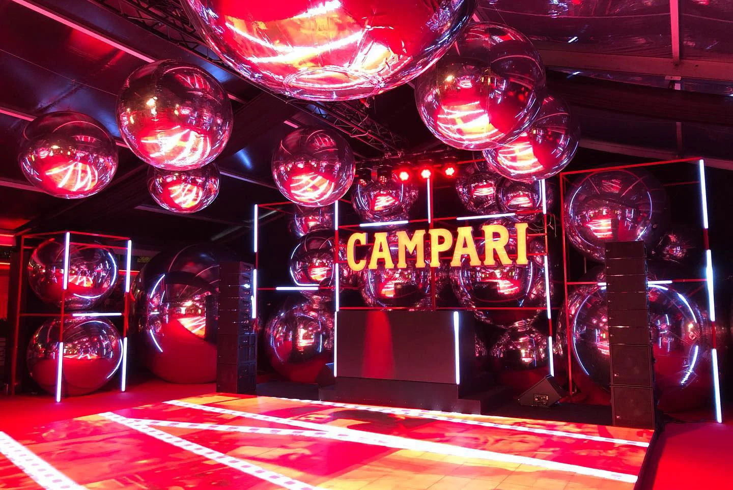 Side view of the dance floor and DJ booth beneath clusters of mirrored spheres and neon frames – Campari at the 75th Cannes Film Festival, France, 2022 – event design