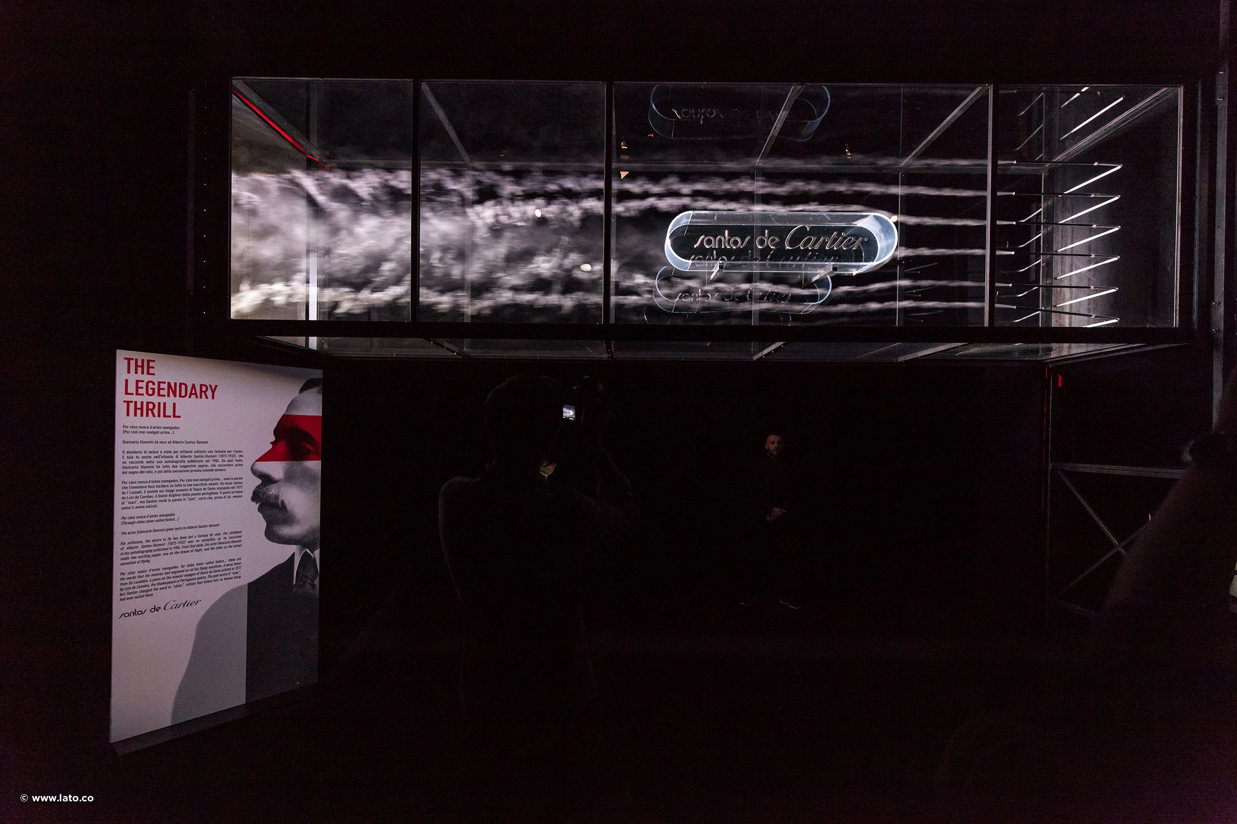 Dark room with a Santos de Cartier sign in a glass case and a lit panel titled The Legendary Thrill – Cartier The Legendary Thrill, Milan, Italy, 2018 – event design