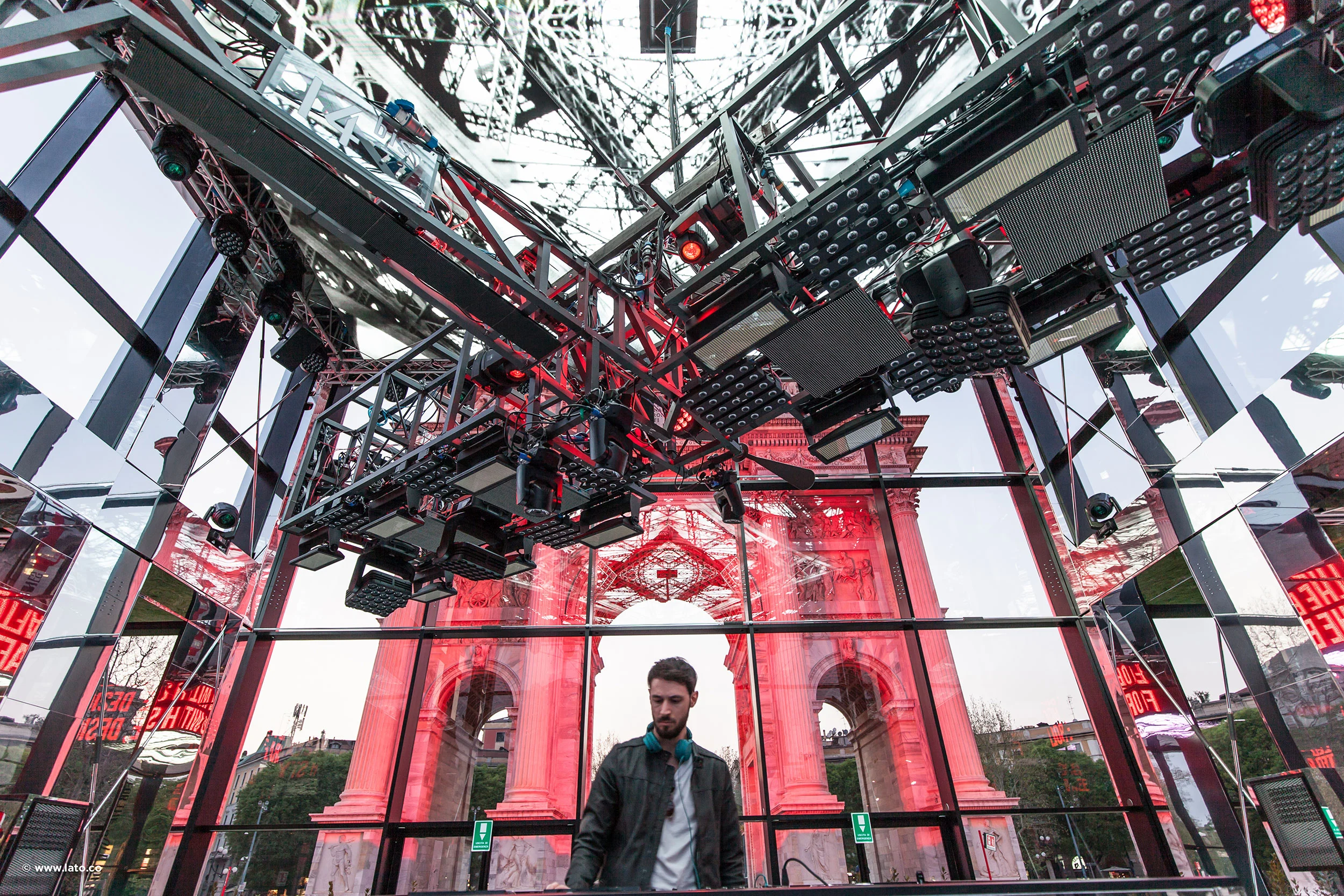 DJ under a red steel truss with light panels, the arch visible through the glass walls – Cartier The Legendary Thrill, Milan, Italy, 2018 – event design