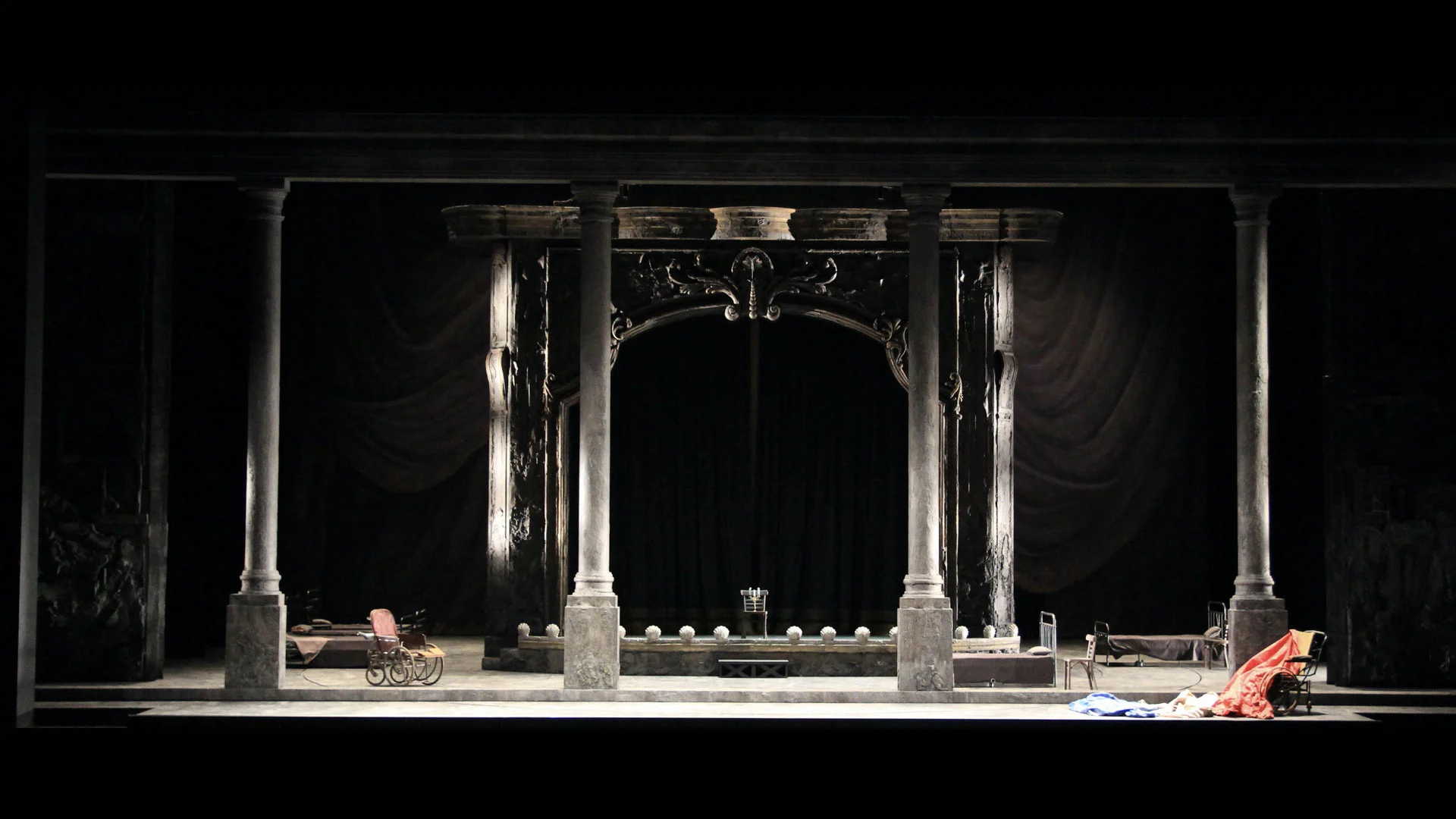 Stage set with tall columns framing an ornate theatre portal, a pram and bed on the dim stage – Adriana Lecouvreur at Opéra de Monte-Carlo, Monte Carlo, Monaco, 2026 – set design