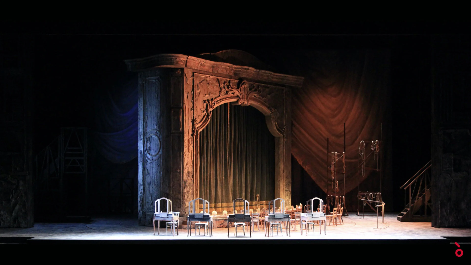 Carved portal with green curtain and red drapes behind, dressing tables lined up in warm light – Adriana Lecouvreur at Opéra de Monte-Carlo, Monte Carlo, Monaco, 2026 – set design