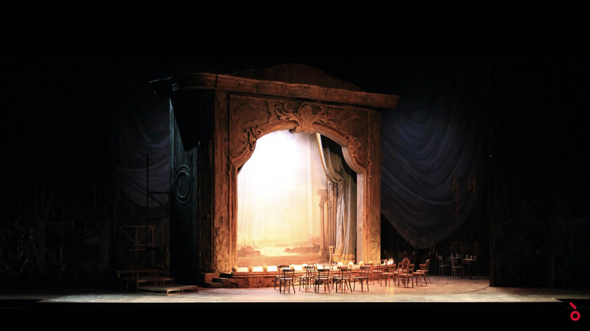 Carved theatre portal glowing with a painted backdrop, café tables and chairs in front – Adriana Lecouvreur at Opéra de Monte-Carlo, Monte Carlo, Monaco, 2026 – set design