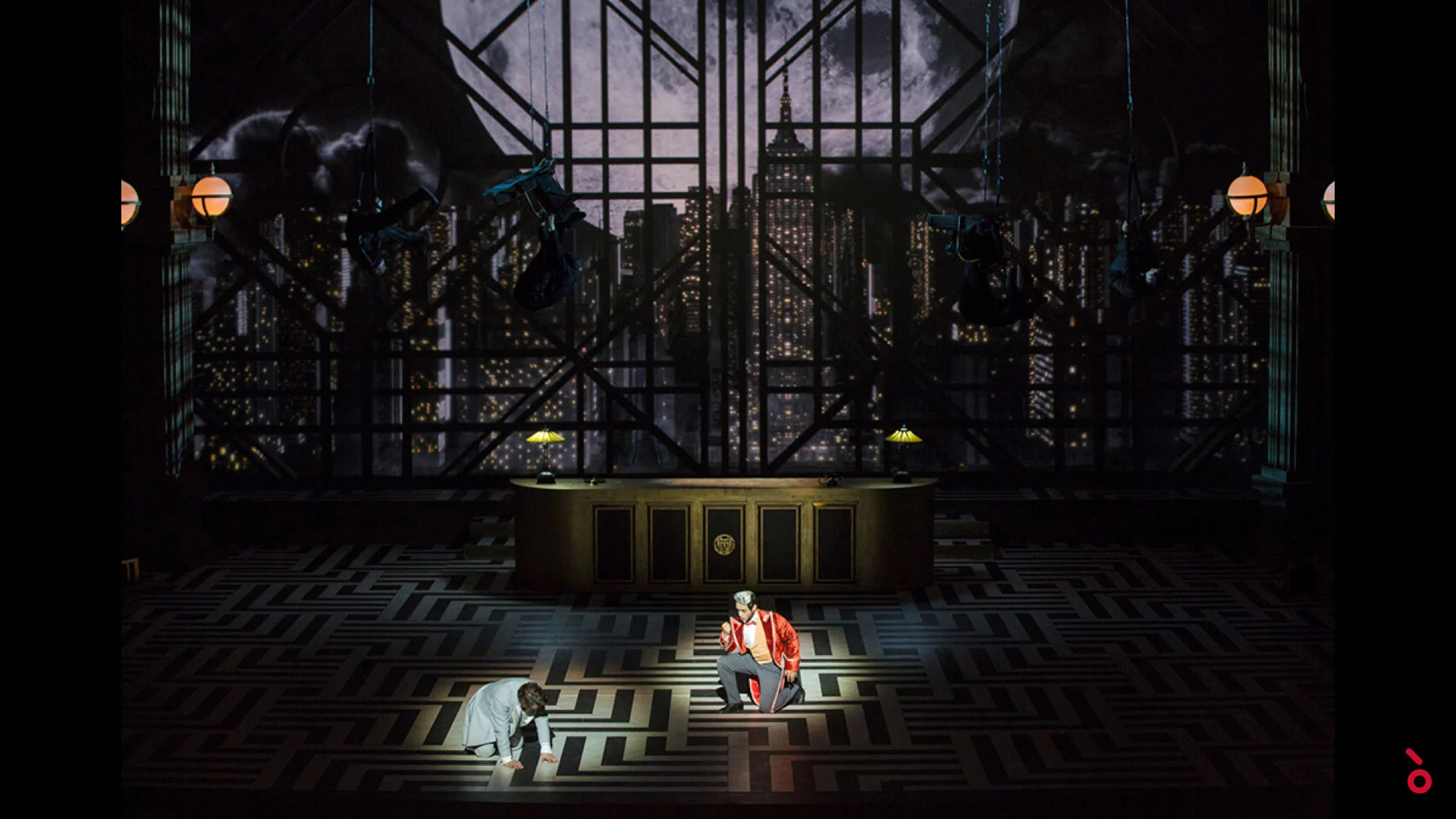 Two performers on a maze floor before a reception desk and a backdrop of night skyscrapers – The Opera! at the Royal Opera House Muscat, Oman, 2019 – set design