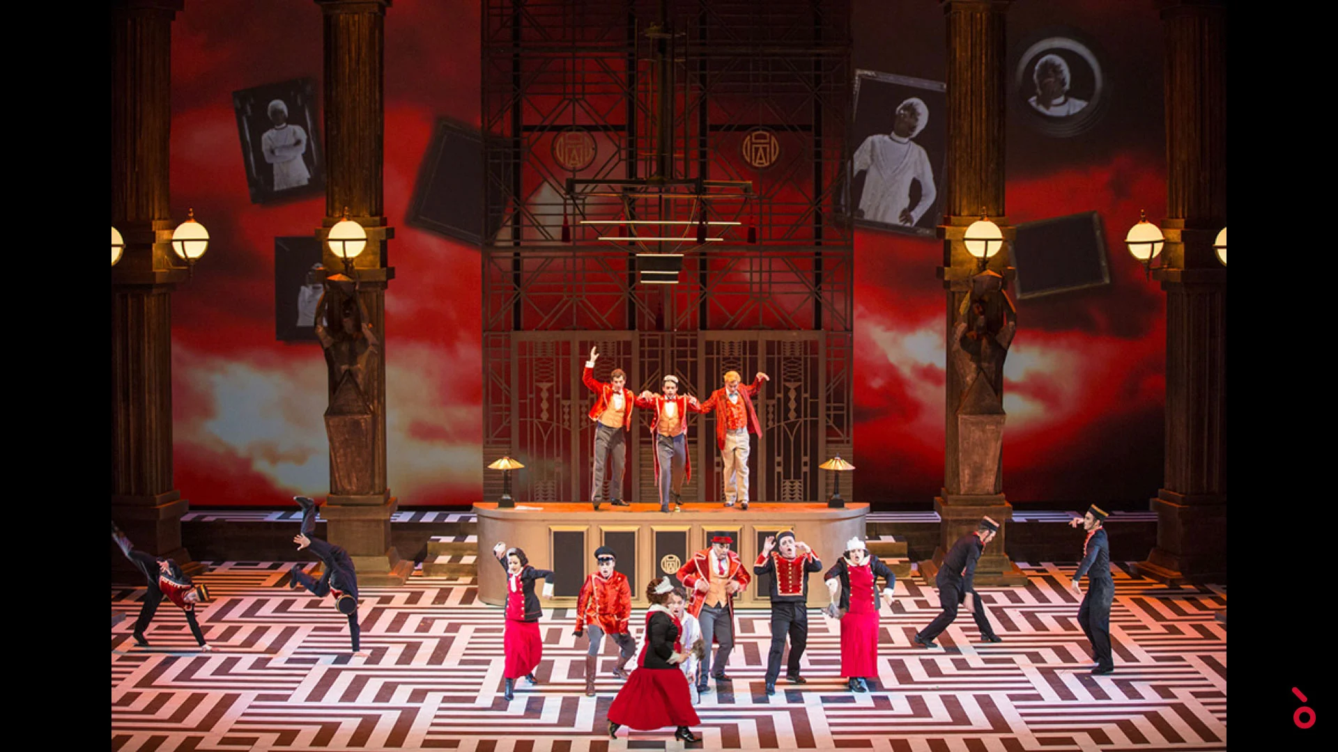 Bellhops dancing on a black and white maze floor before a red sky backdrop with floating portraits – The Opera! at the Royal Opera House Muscat, Oman, 2019 – set design