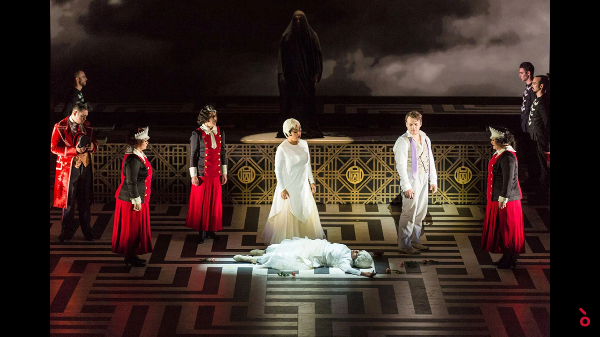 Cast in red and white costumes around a figure lying on a geometric floor, a veiled statue above – The Opera! at the Royal Opera House Muscat, Oman, 2019 – set design