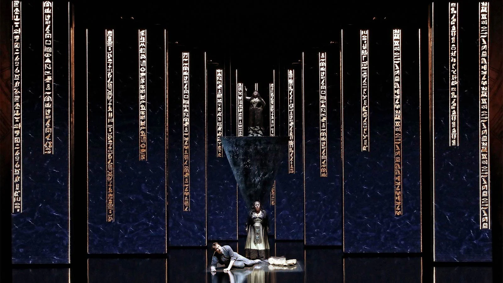 Deep blue screens with columns of gold hieroglyphs, a woman standing and a man fallen on the floor – Aida at Sydney Opera House, Australia, 2018 – set design
