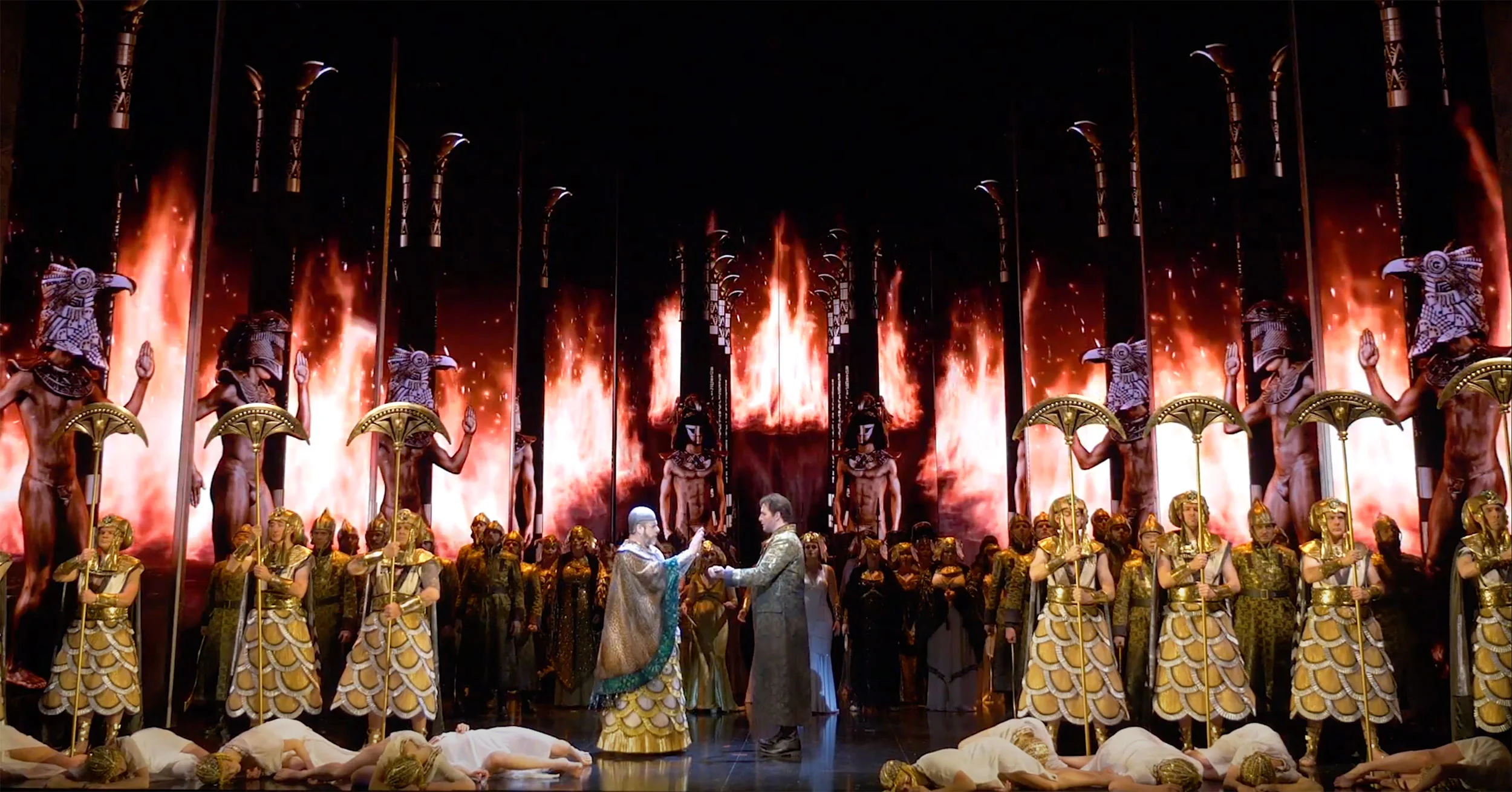 Triumphal scene with guards and dancers before gold statues and video screens showing flames – Aida at Sydney Opera House, Australia, 2018 – set design