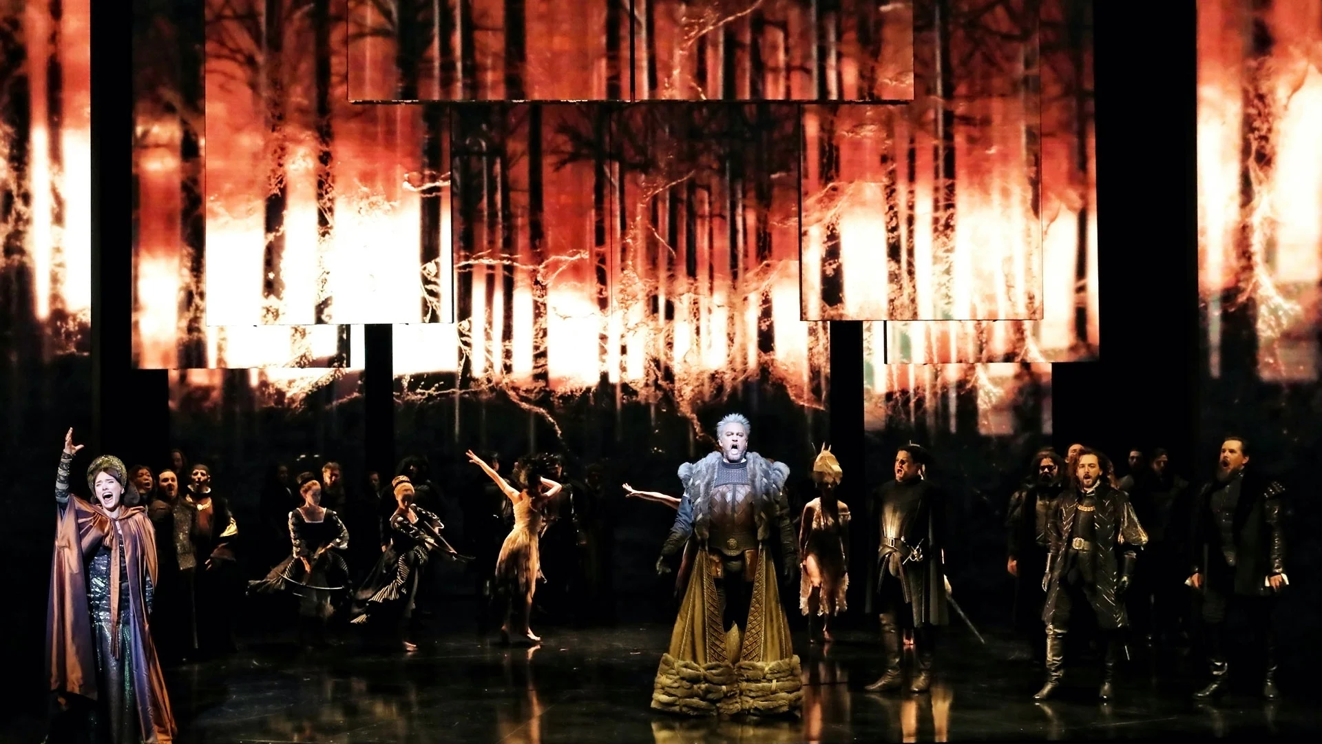 Anna Bolena on stage: queen in a gold gown before the cast, under burning forest projections on hanging panels – Anna Bolena at Sydney Opera House, Australia, 2019 – set design