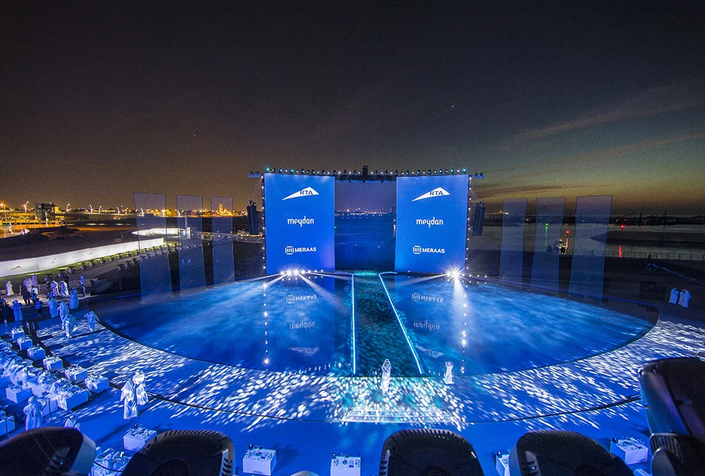 Wide view of the floating stage at dusk: blue water floor, sponsor screens and guest seating along the shore – Dubai Water Canal Opening Ceremony, United Arab Emirates, 2016 – event design