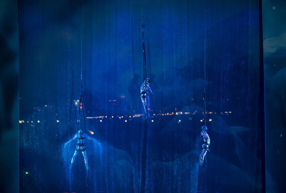 Close-up of three aerial performers hanging on ropes in front of a falling curtain of water, lit in blue – Dubai Water Canal Opening Ceremony, United Arab Emirates, 2016 – event design