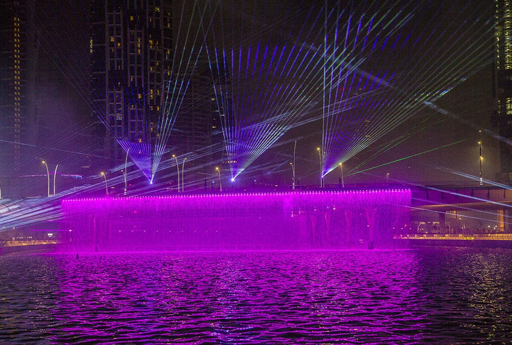 Waterfall wall glowing magenta under fans of laser beams, reflected in the Dubai Water Canal at night – Dubai Water Canal Opening Ceremony, United Arab Emirates, 2016 – event design