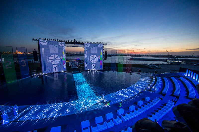 Rehearsal at sunset: test patterns on the screens, illuminated water stage and empty white seats – Dubai Water Canal Opening Ceremony, United Arab Emirates, 2016 – event design