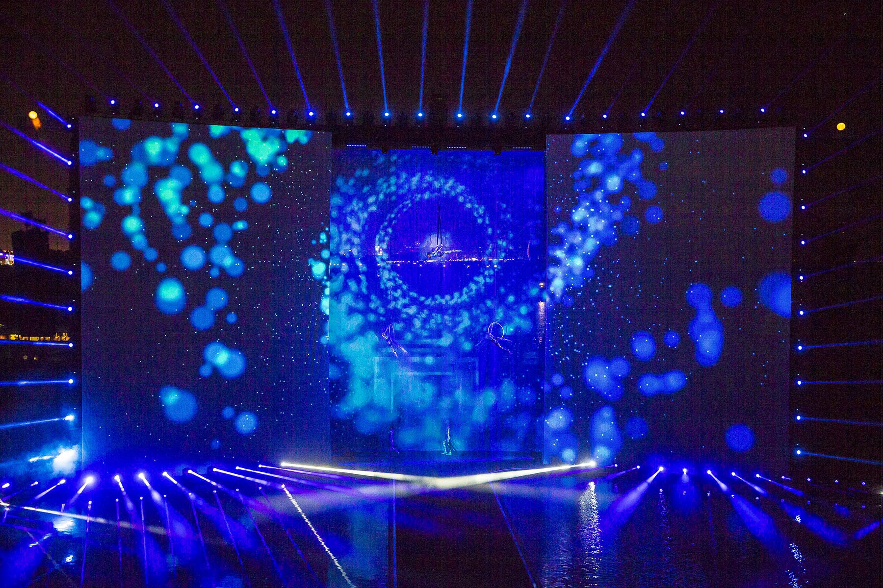 Front view of the stage with blue bubble projections across three screens and a central swirling vortex – Dubai Water Canal Opening Ceremony, United Arab Emirates, 2016 – event design