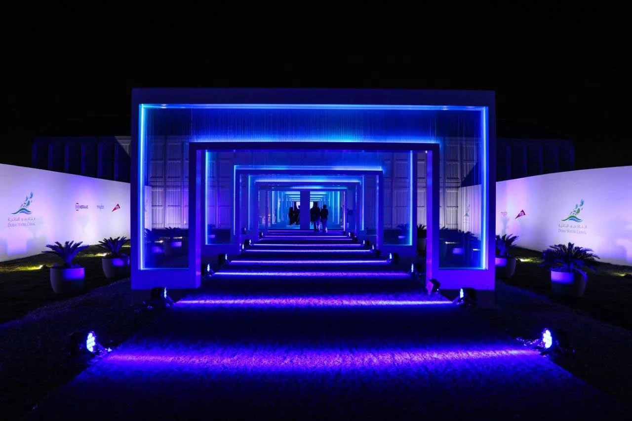 Guest entrance through a tunnel of nested blue-lit frames, flanked by palms and white walls – Dubai Water Canal Opening Ceremony, United Arab Emirates, 2016 – event design