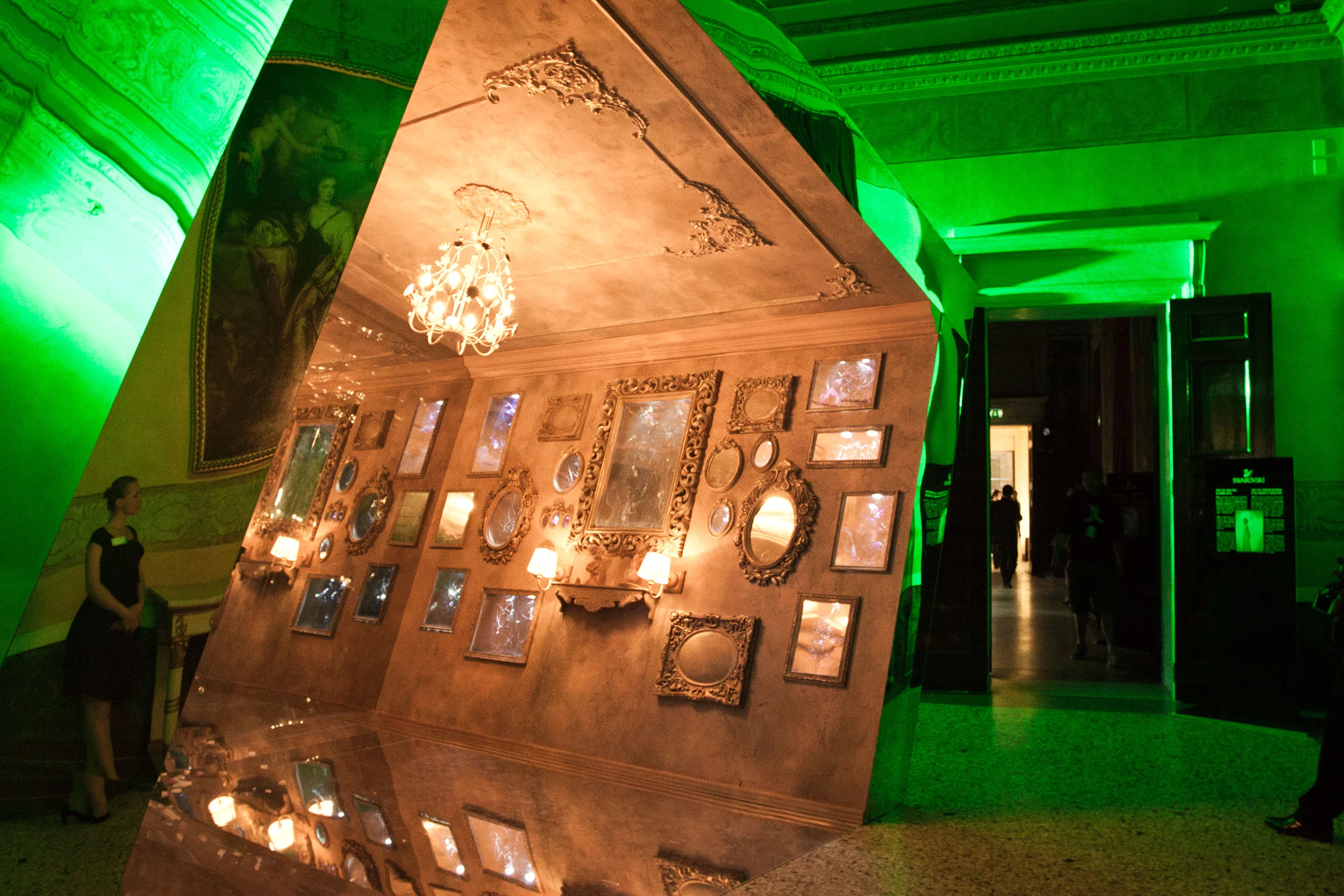 Angled mirrored panel reflecting a room of gilded frames and a chandelier, in a green-lit hall – Swarovski Fashionation Party at Palazzo Reale, Milan, Italy, 2011 – event design