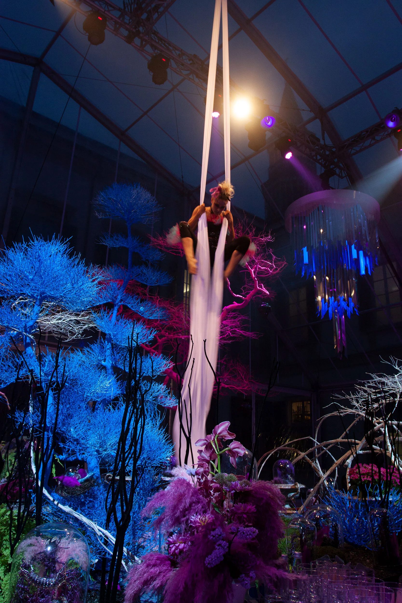 Aerial acrobat on white silks above blue and purple feathered trees and floral installations – Swarovski Fashionation Party at Palazzo Reale, Milan, Italy, 2011 – event design