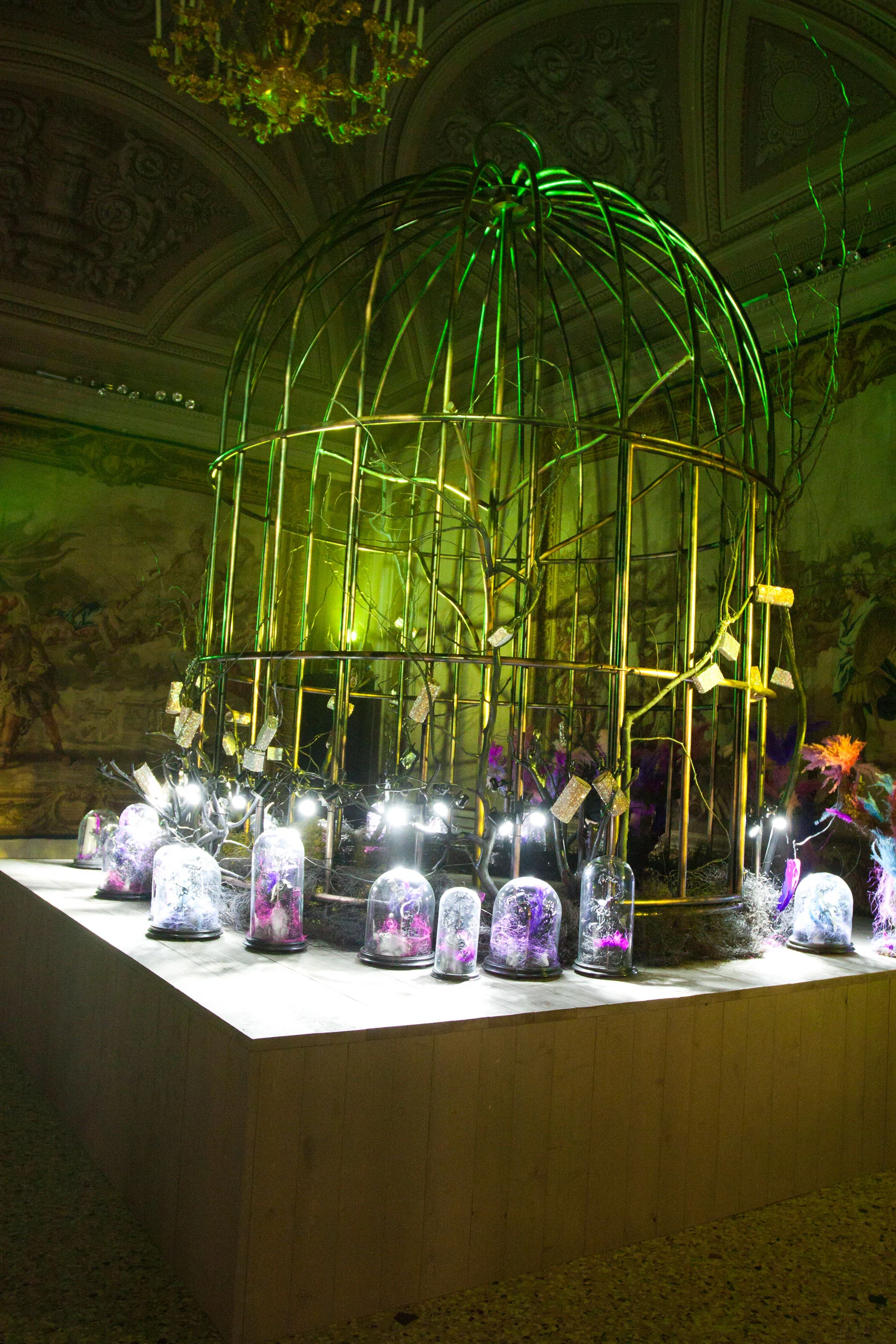 Golden birdcage under green light in a frescoed hall, surrounded by glass domes holding purple jewels – Swarovski Fashionation Party at Palazzo Reale, Milan, Italy, 2011 – event design