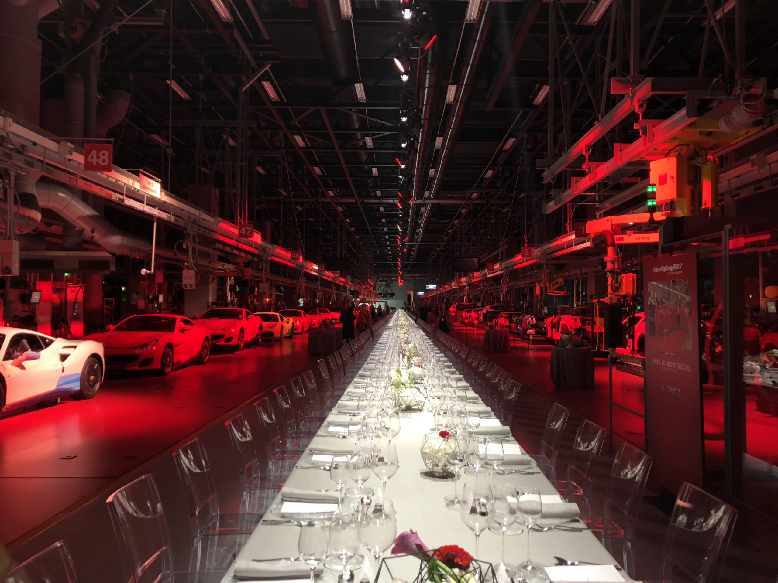 Long dinner table set in a red-lit factory hall, Ferrari cars parked along the sides – Ferrari Monza SP1 Unveiling, Maranello, Italy, 2018 – event design