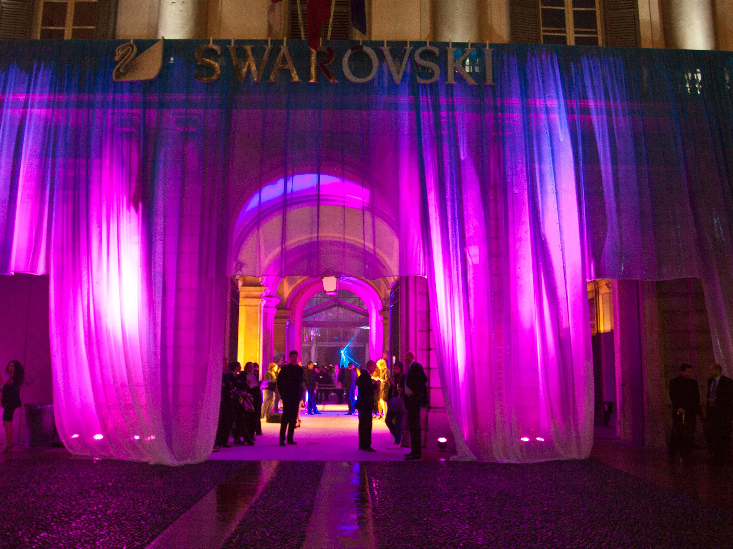 Palazzo Reale entrance draped in sheer curtains lit magenta, with the Swarovski logo above the arched doorway at night – Swarovski Fashionation Party at Palazzo Reale, Milan, Italy, 2011 – event design