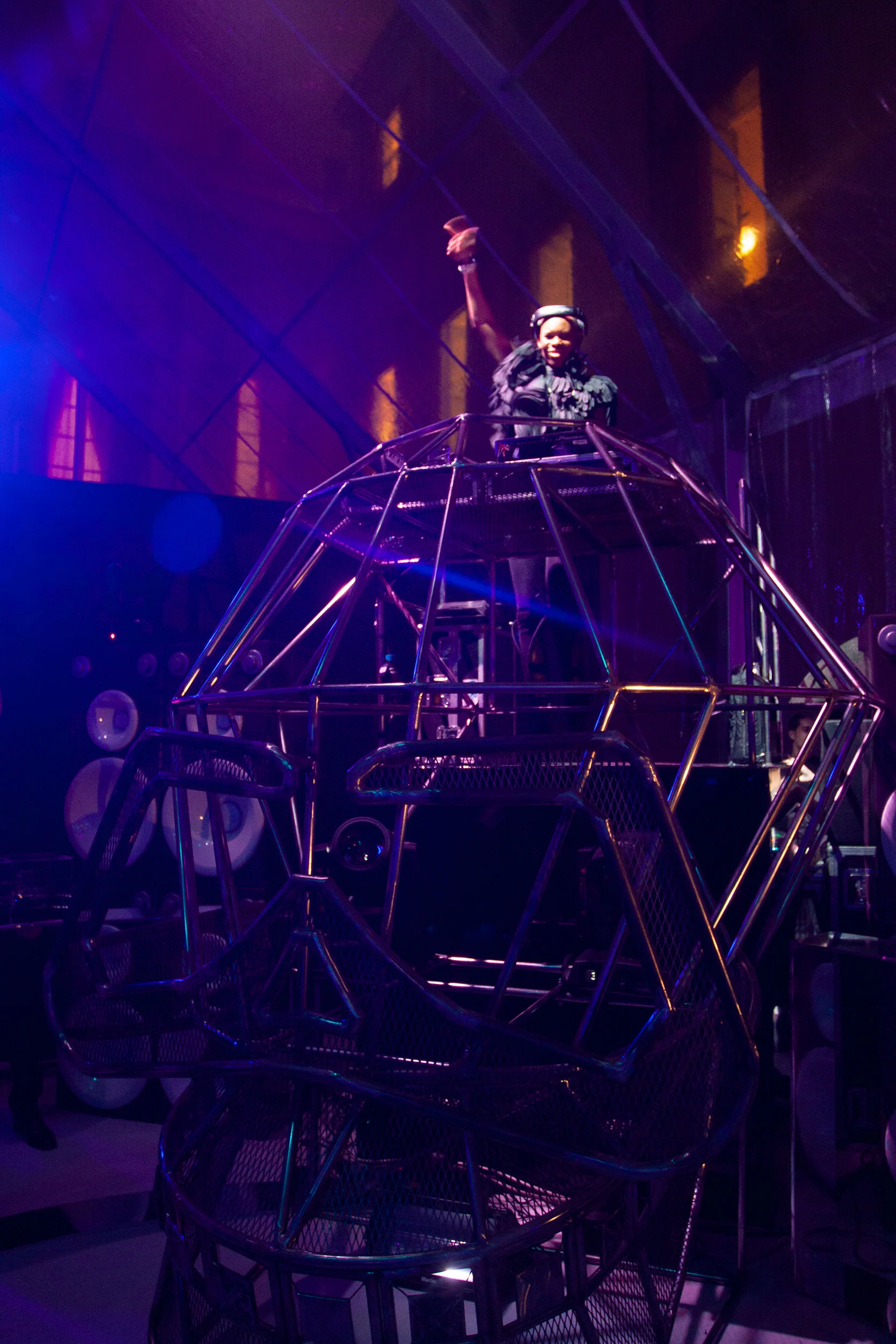 DJ raising an arm atop a tall geometric metal-frame booth shaped like a head, lit in violet – Swarovski Fashionation Party at Palazzo Reale, Milan, Italy, 2011 – event design