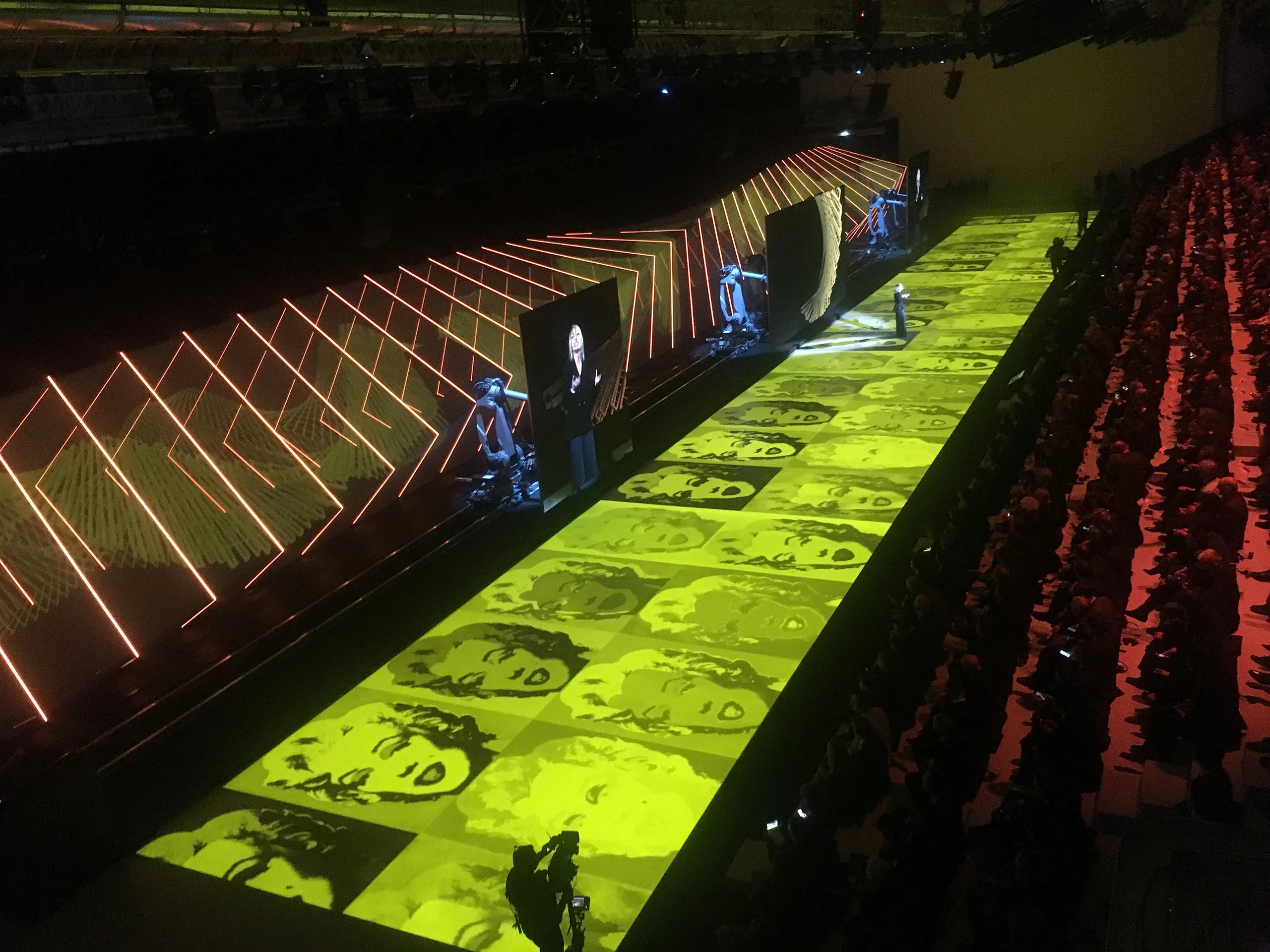 Long runway lit in yellow with projected pop-art faces, robotic arms and orange light frames beside the audience – Lamborghini Urus World Premiere, Sant'Agata Bolognese, Italy, 2017 – event design