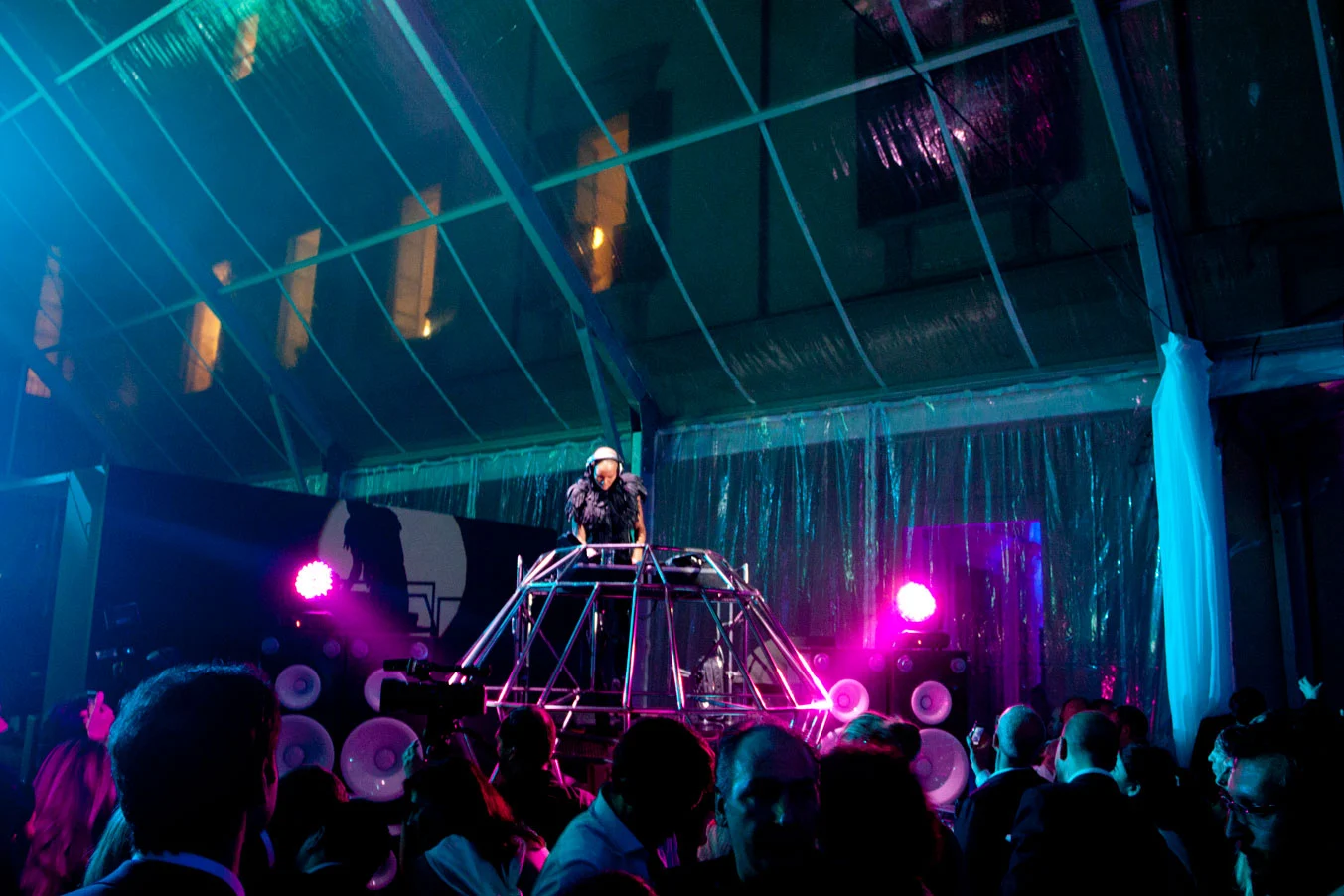 DJ playing from a metal-frame booth under a transparent tent roof, crowd lit in pink and teal – Swarovski Fashionation Party at Palazzo Reale, Milan, Italy, 2011 – event design