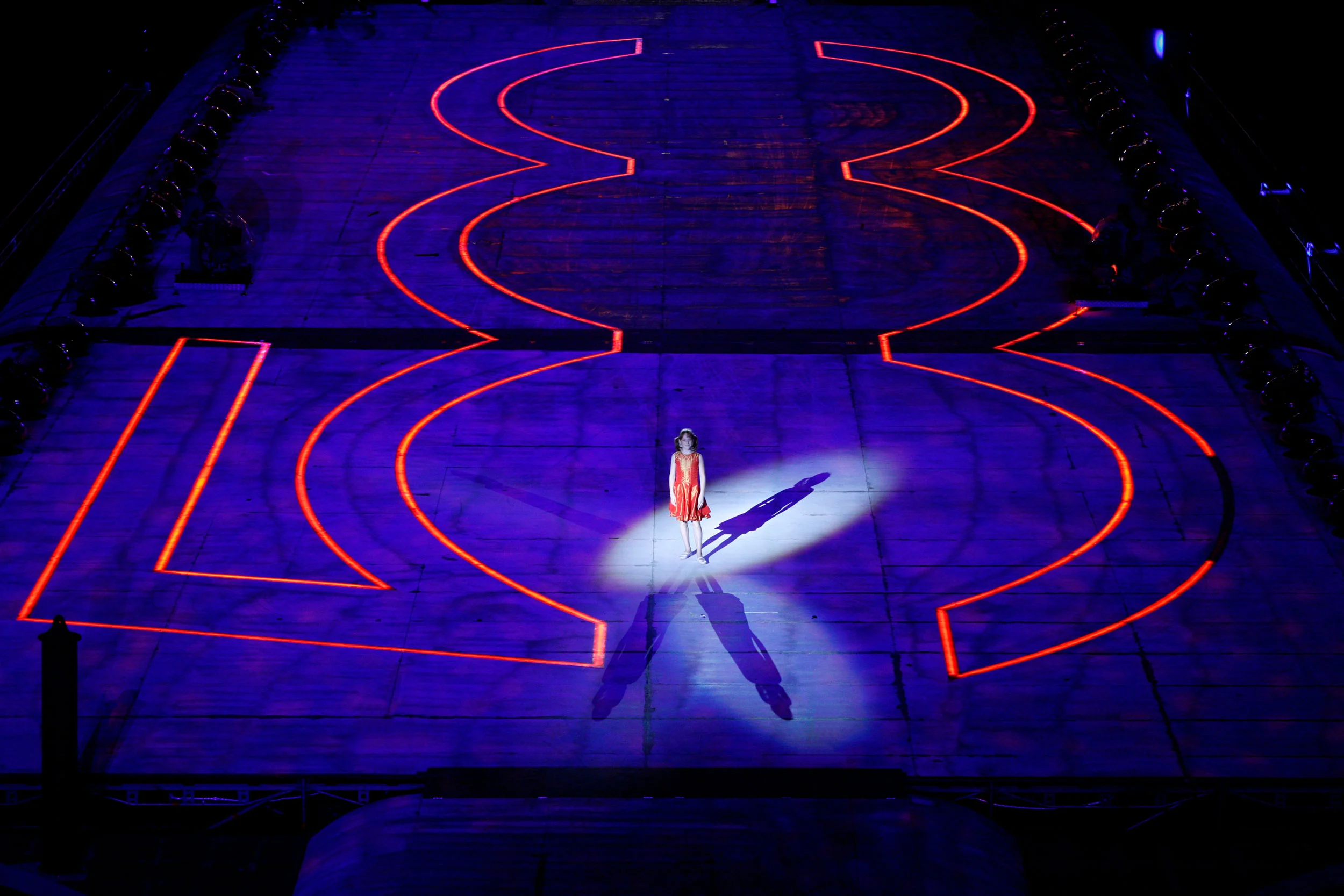 Aerial view of a performer in red standing in a spotlight on a stage marked with a giant red 500 outline – Fiat Welcome 500 World Premiere, Turin, Italy, 2007 – event design