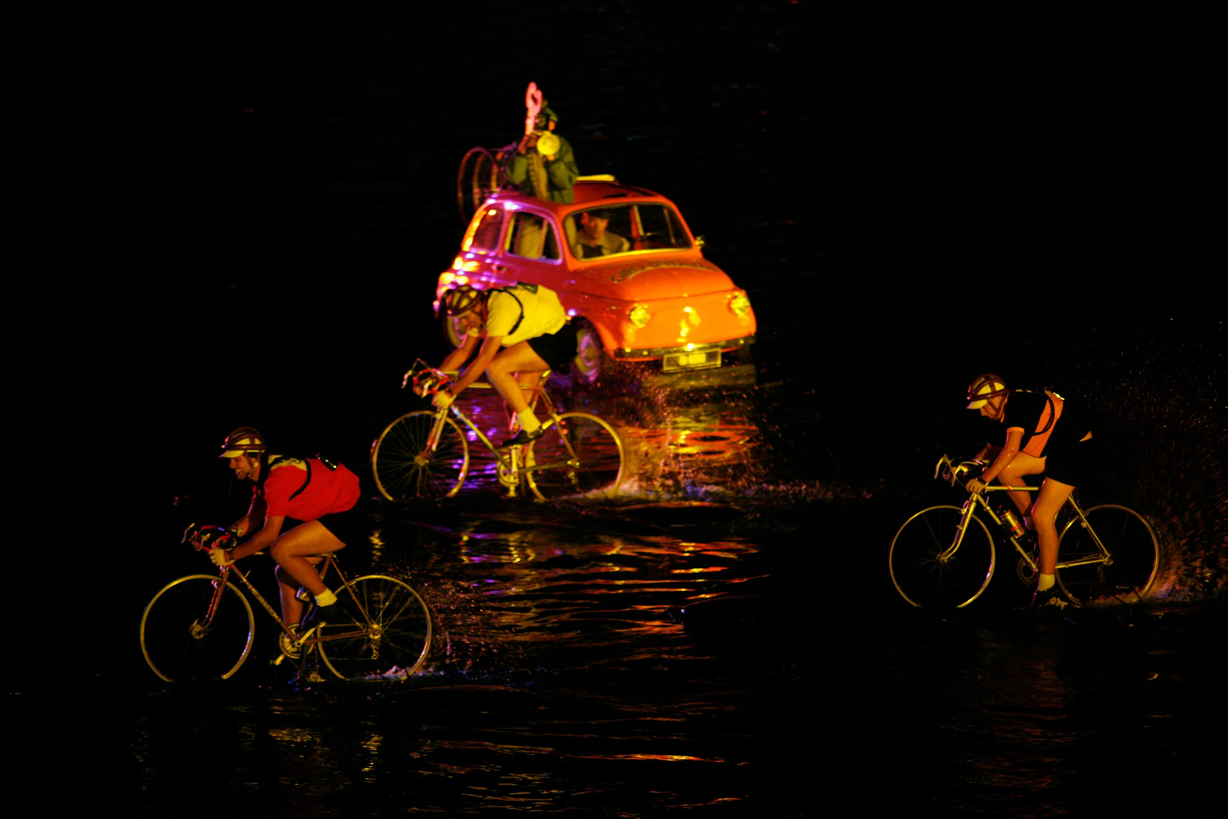 Cyclists in vintage racing jerseys riding through water in front of an orange classic Fiat 500 at night – Fiat Welcome 500 World Premiere, Turin, Italy, 2007 – event design