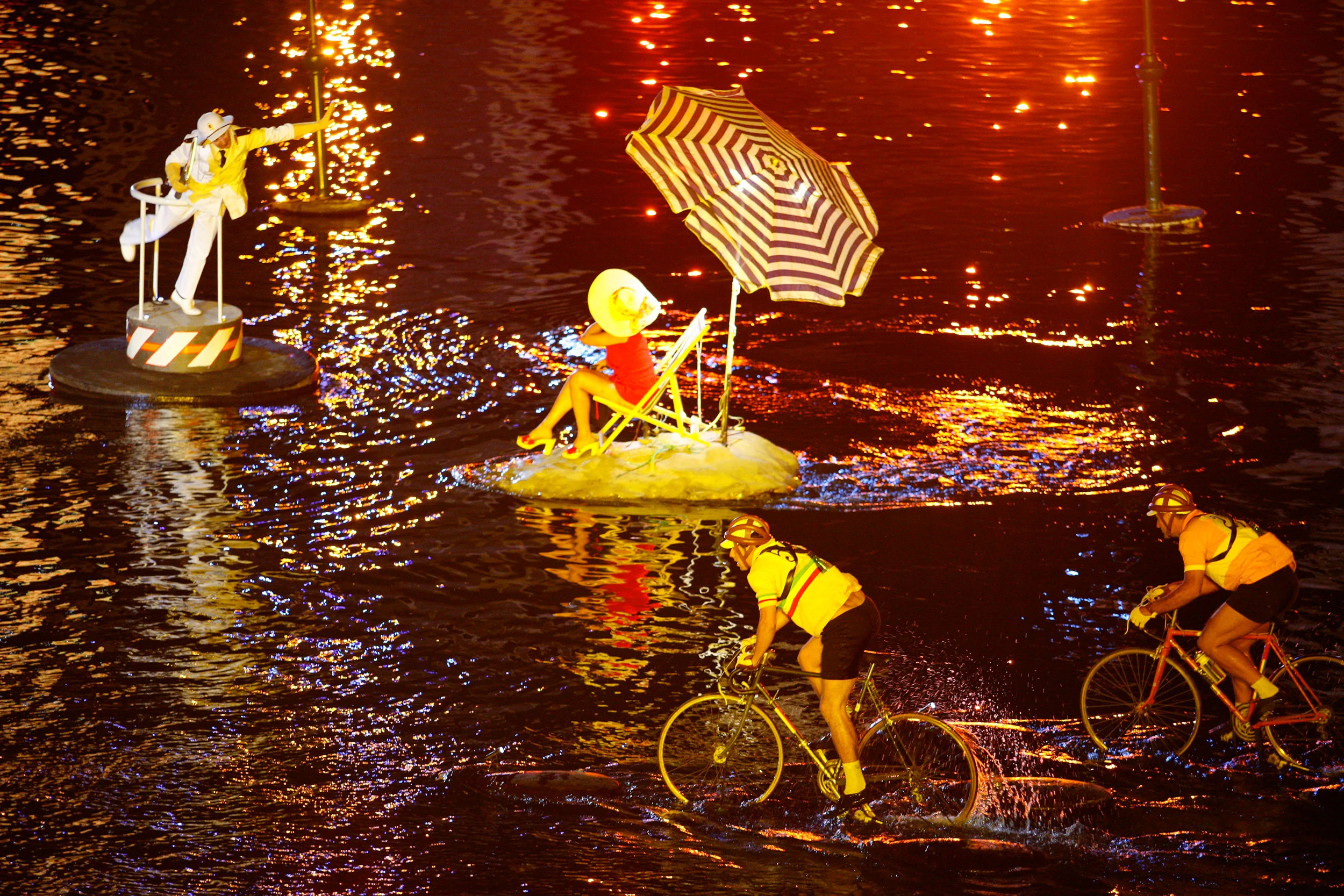 Performers on floating islands with a striped beach umbrella and deckchair, cyclists splashing through the river – Fiat Welcome 500 World Premiere, Turin, Italy, 2007 – event design