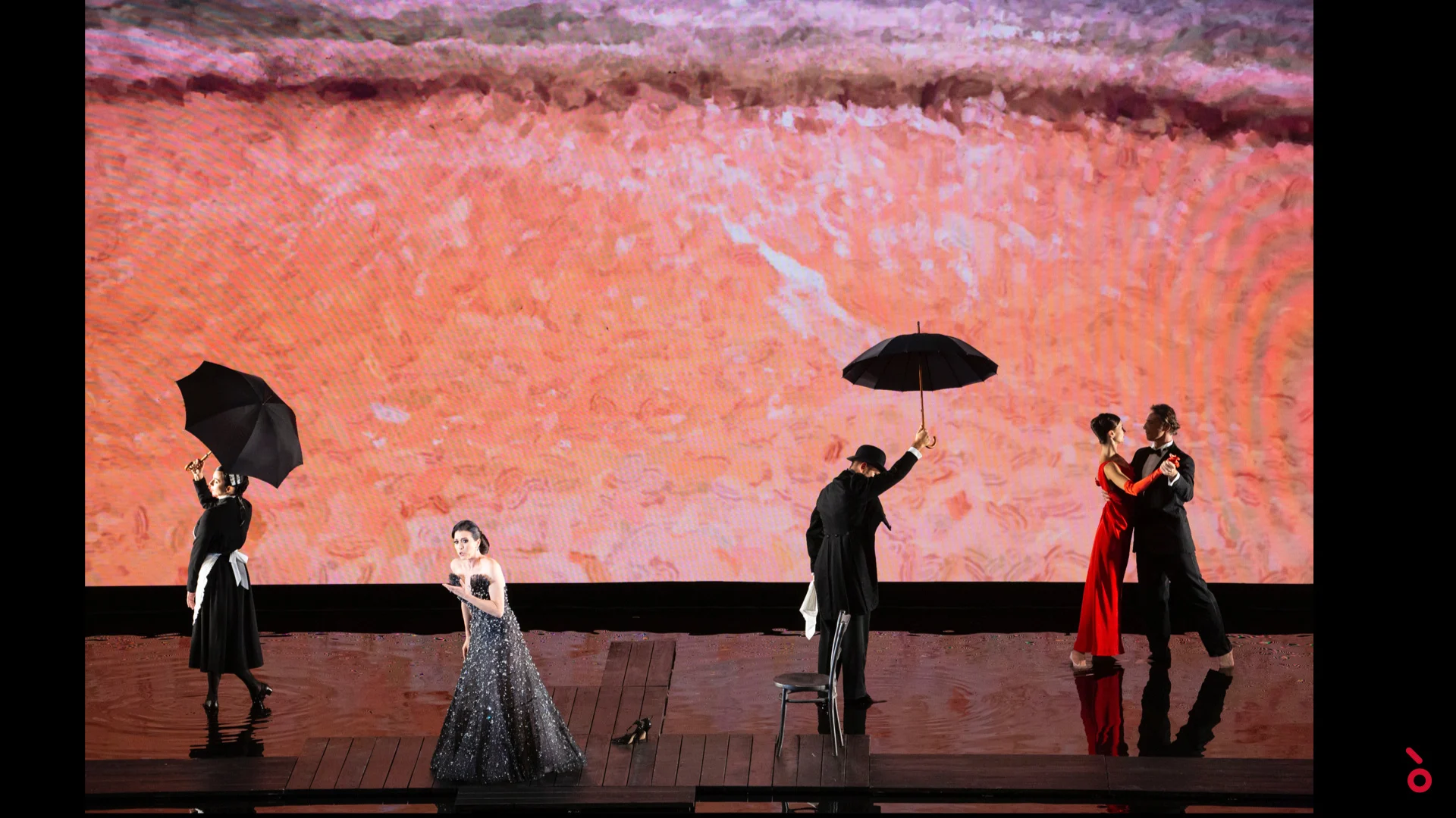 Performers with black umbrellas and a dancing couple on a wooden platform before a coral-red projection – A Riveder le Stelle at La Scala, Milan, Italy, 2020 – opera set design
