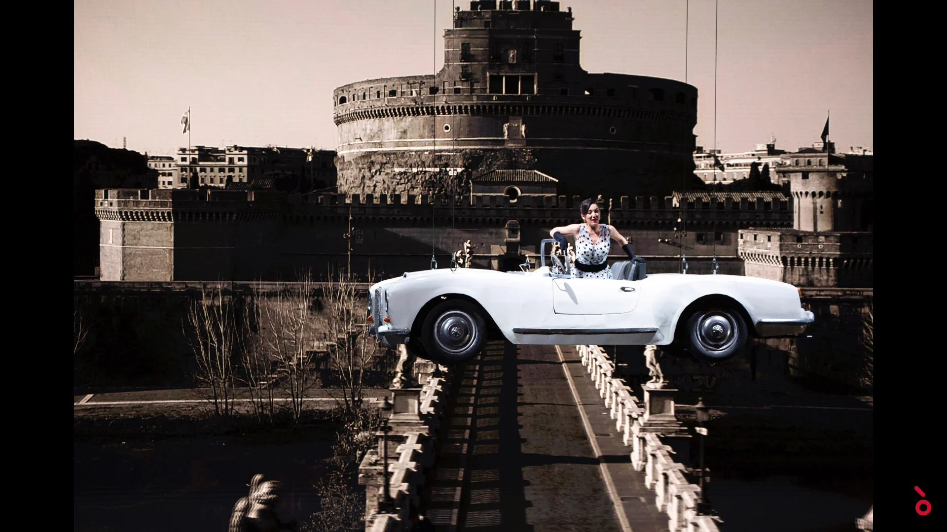 Singer in a white convertible that seems to float over a bridge, Castel Sant'Angelo projected behind – A Riveder le Stelle at La Scala, Milan, Italy, 2020 – opera set design