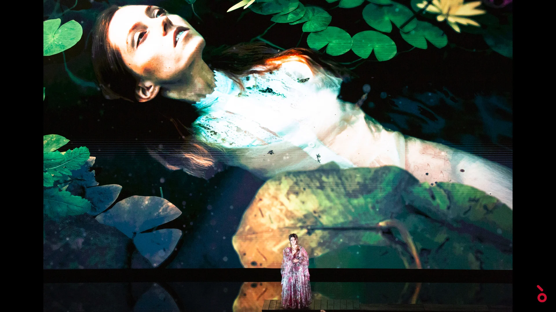 Singer in a long gown dwarfed by a projection of a woman floating among water lilies – A Riveder le Stelle at La Scala, Milan, Italy, 2020 – opera set design