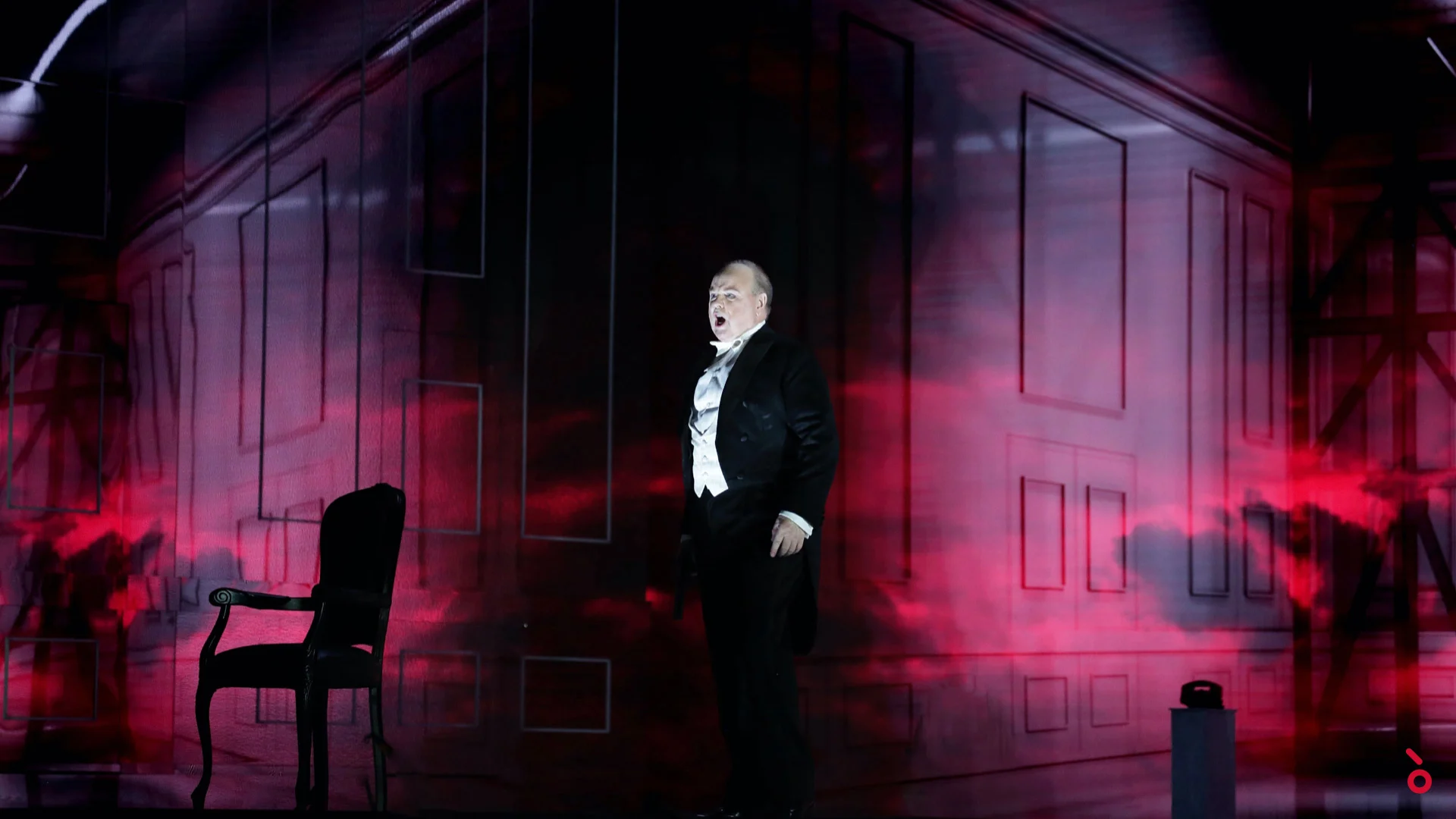 Singer in tailcoat beside an empty chair, palace walls projected in red mist behind him – Elisabetta, Regina d'Inghilterra at Rossini Opera Festival, Pesaro, Italy, 2021 – set design
