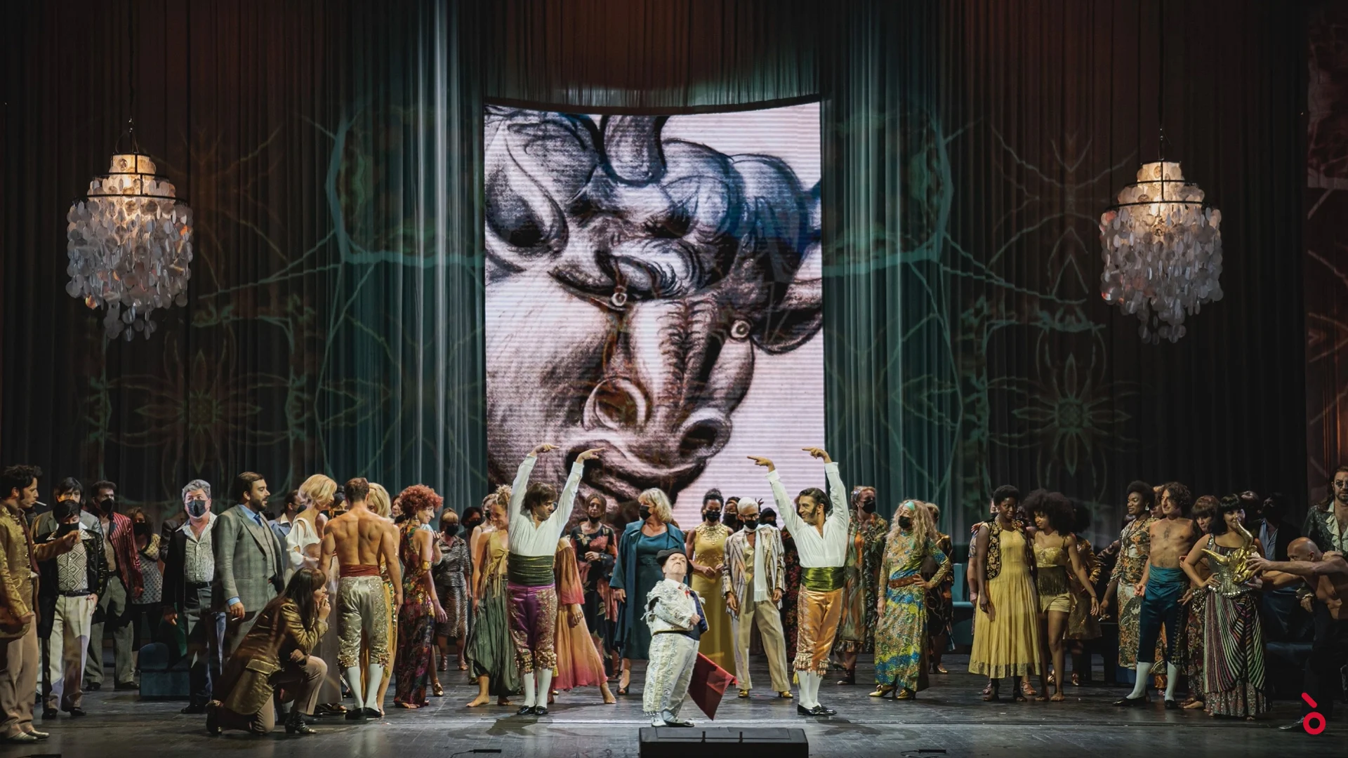Chorus in colourful 1960s dress before a giant projected bull drawing, crystal chandeliers on either side – La Traviata at Maggio Musicale Fiorentino, Florence, Italy, 2022 – opera set design